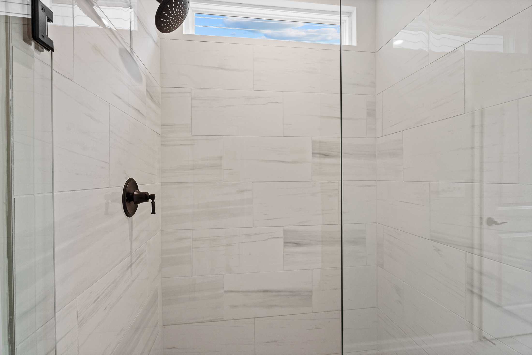 Modern walk-in shower in The Glenwood B master suite featuring white subway tile, frameless glass enclosure, rainfall showerhead, and transom window