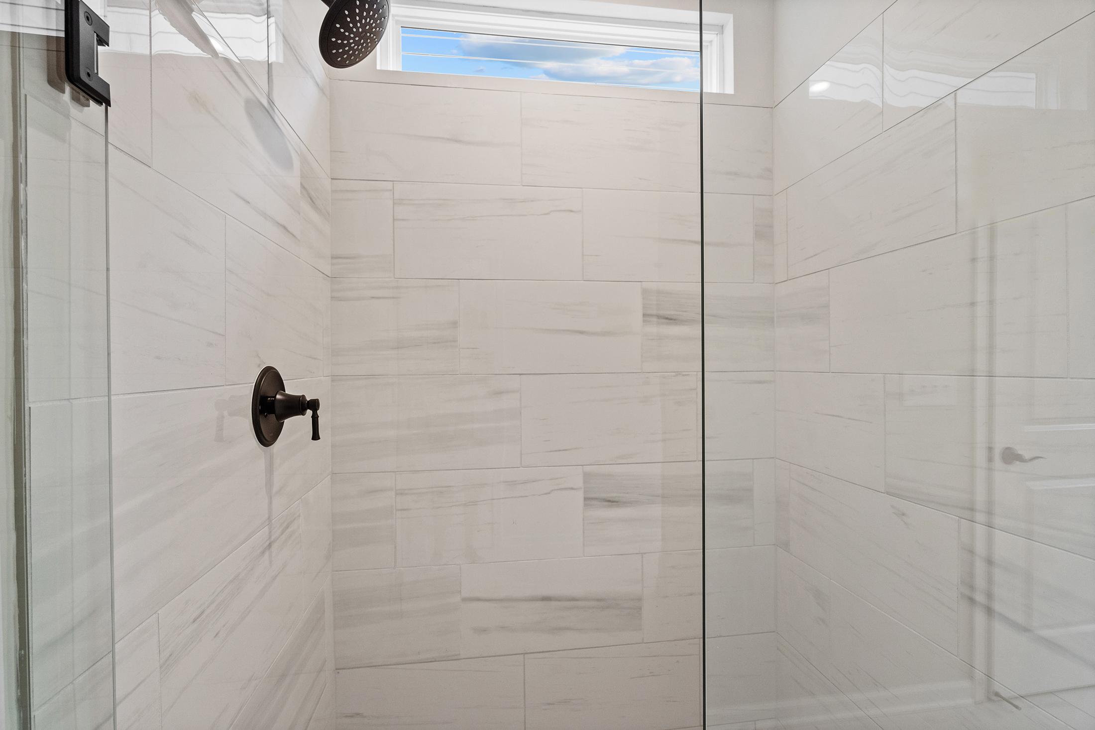 Spacious walk-in shower in The Glenwood master bathroom featuring white subway tile walls, frameless glass enclosure, bronze fixtures, and clerestory window