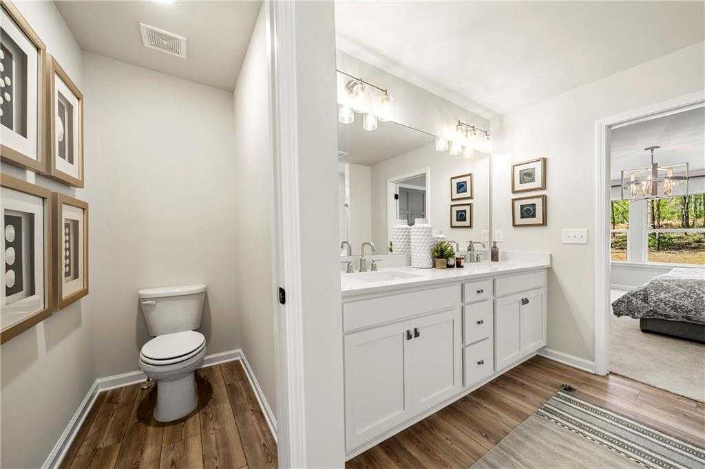 Modern master bathroom with double sink vanity, white cabinets, toilet, framed art, and bedroom view in The Hickory B, Riverwood, Dallas, GA