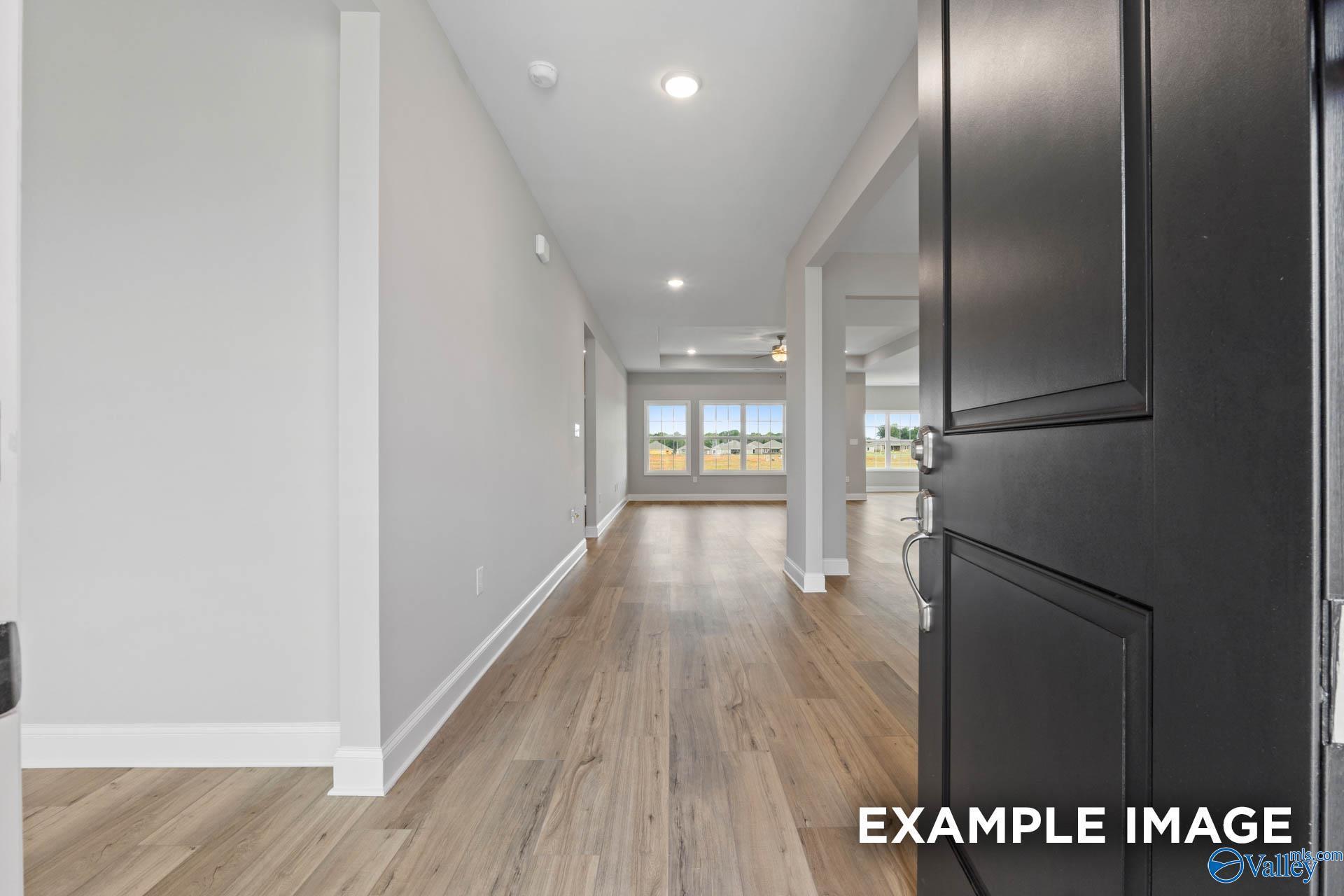 Inviting entry hallway with open black door, light hardwood floors, and large backyard-view windows in Davidson Homes The Finleigh, Harvest AL
