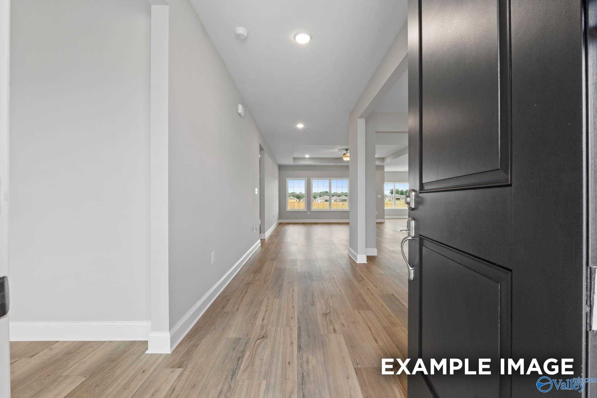 Inviting entry hallway with open black door, light hardwood floors, and large backyard-view windows in Davidson Homes The Finleigh, Harvest AL