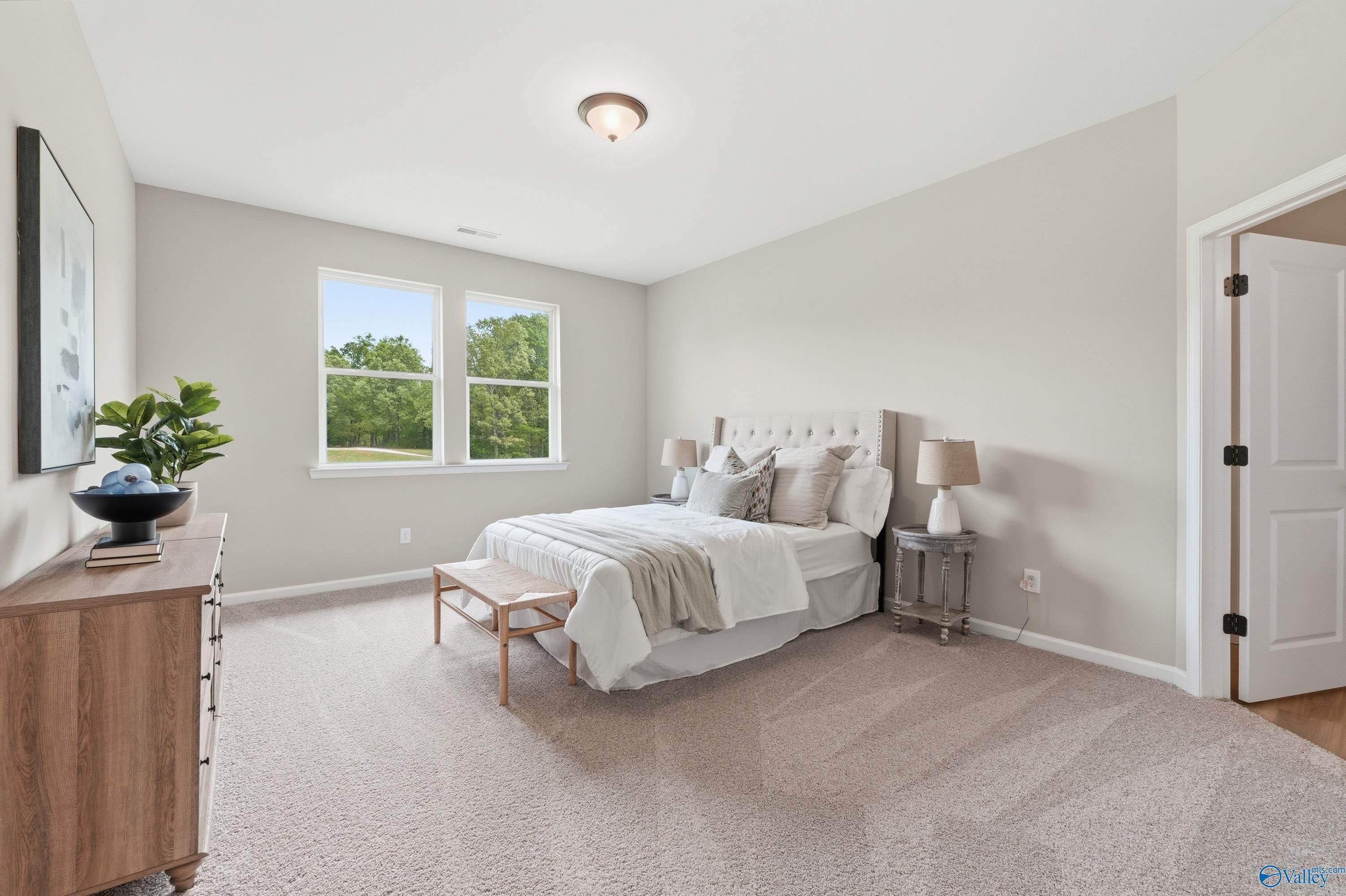 Elegant master bedroom with tufted bed, beige carpet, and tree-view window in Davidson Homes The Dorado, Huntsville