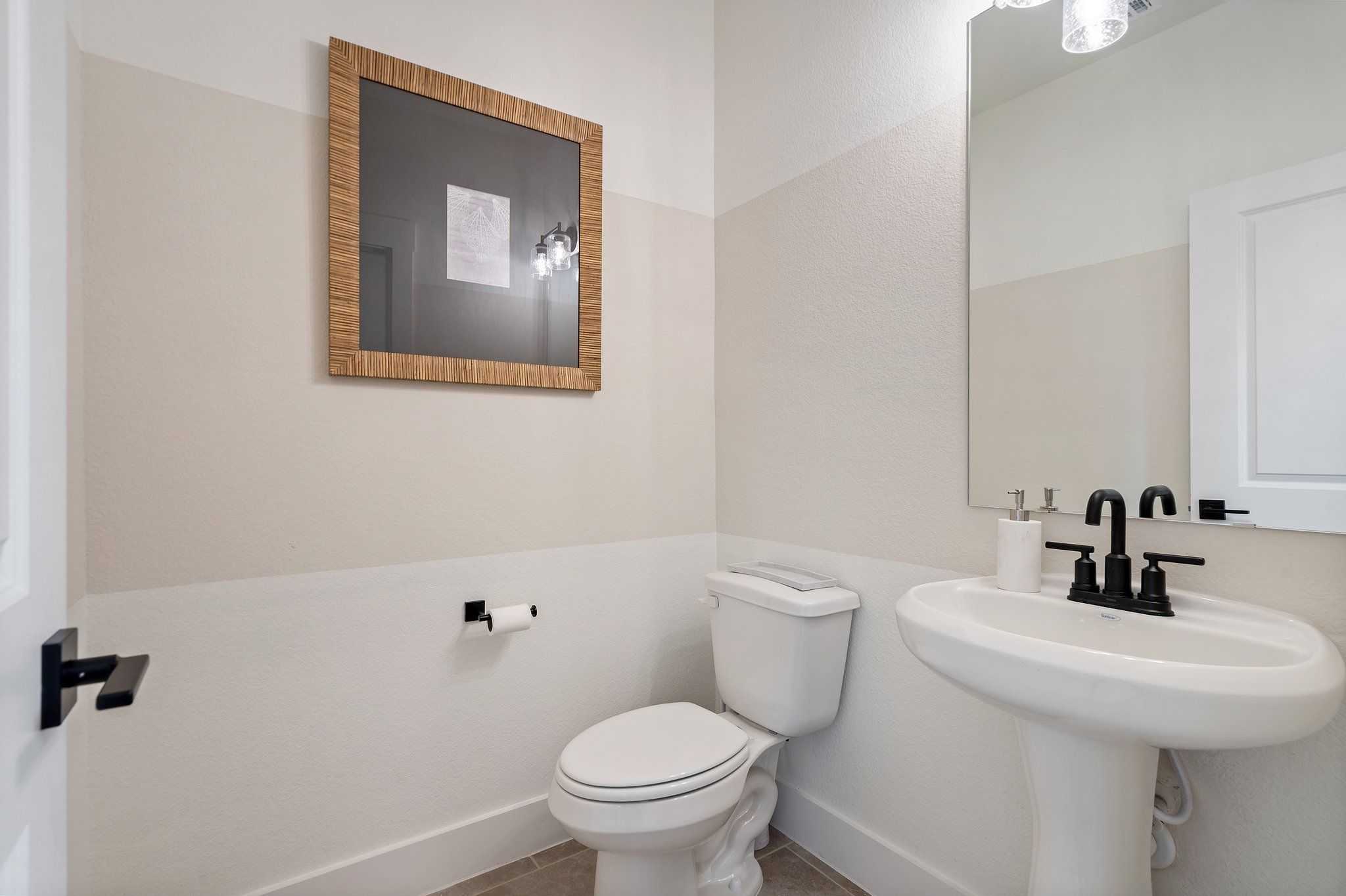 Elegant powder room with pedestal sink, black fixtures, toilet and framed artwork in Davidson Homes The Wake C, Wylie, Texas