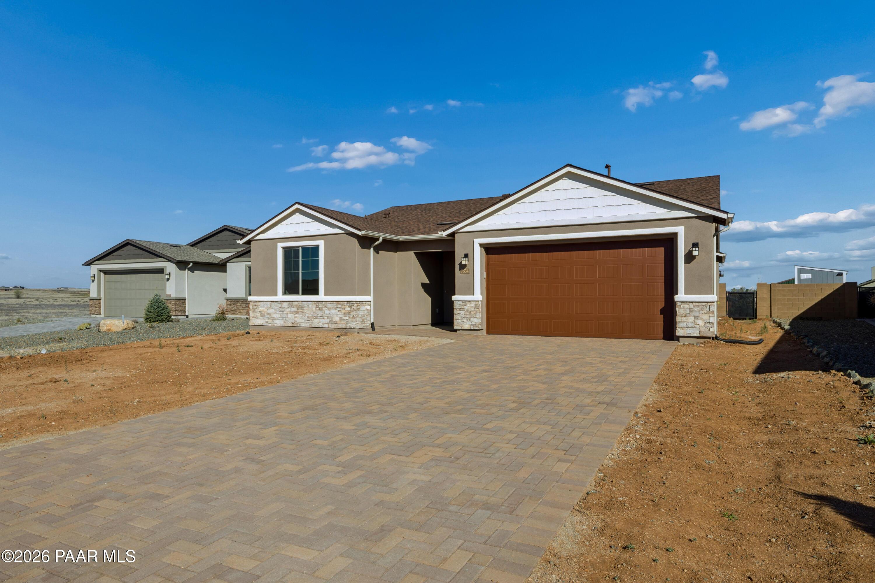 Modern tan stucco single-story home with 3-car garage, paver driveway, and desert landscaping in North Ridge at Pronghorn Ranch, Prescott Valley, Arizona