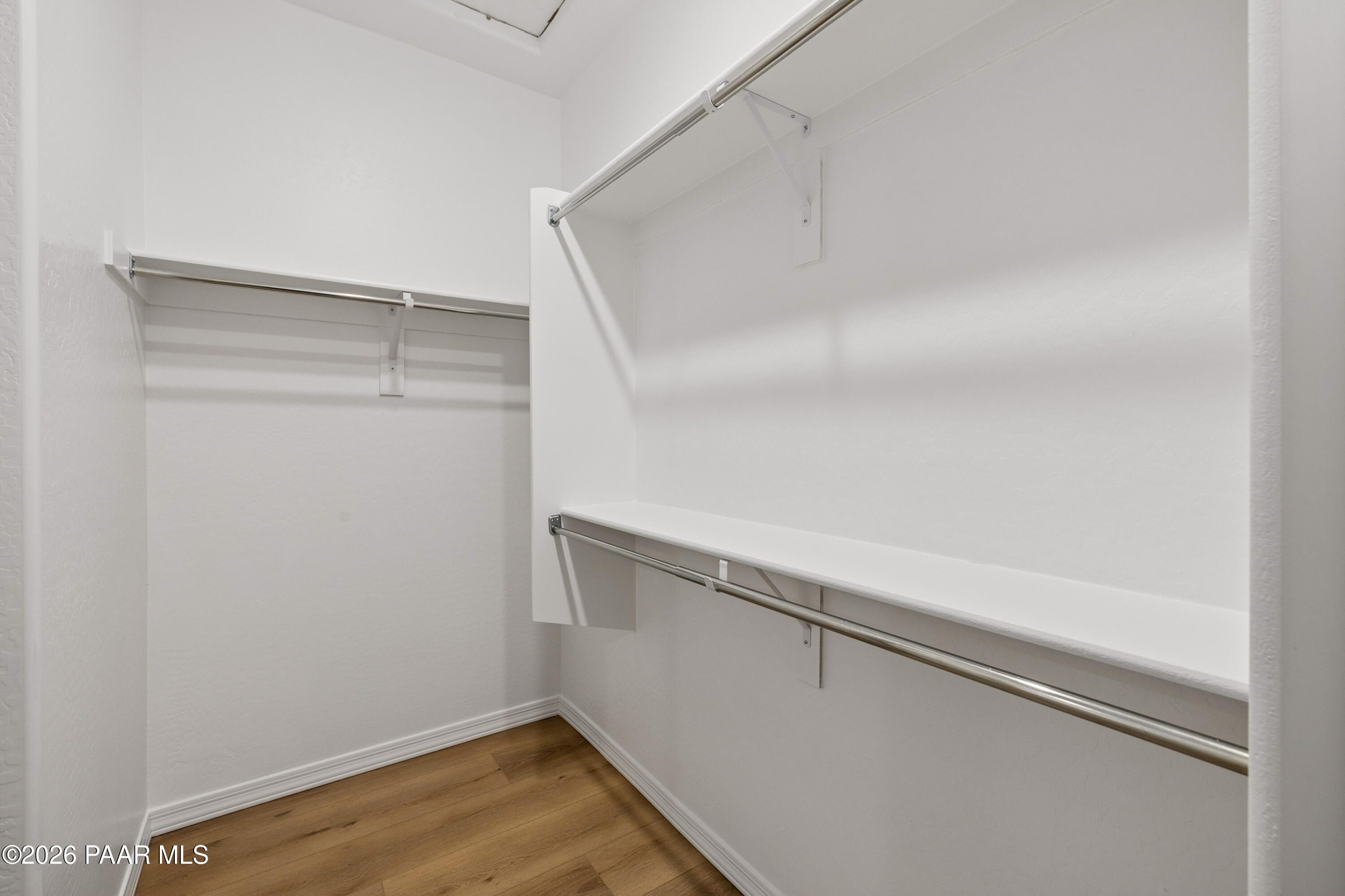 Spacious walk-in closet with double hanging rods, shelving, white walls, and wood-look flooring in Davidson Homes The Harmony A, Prescott Valley, AZ