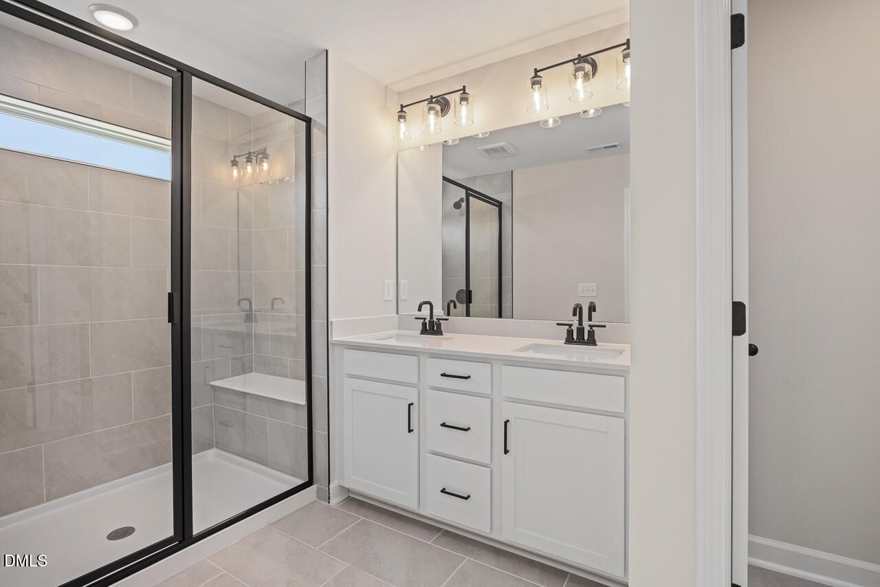 Modern bathroom with double vanity, white cabinets, and walk-in shower in The Mitchell floor plan at Camden Park, Knightdale.