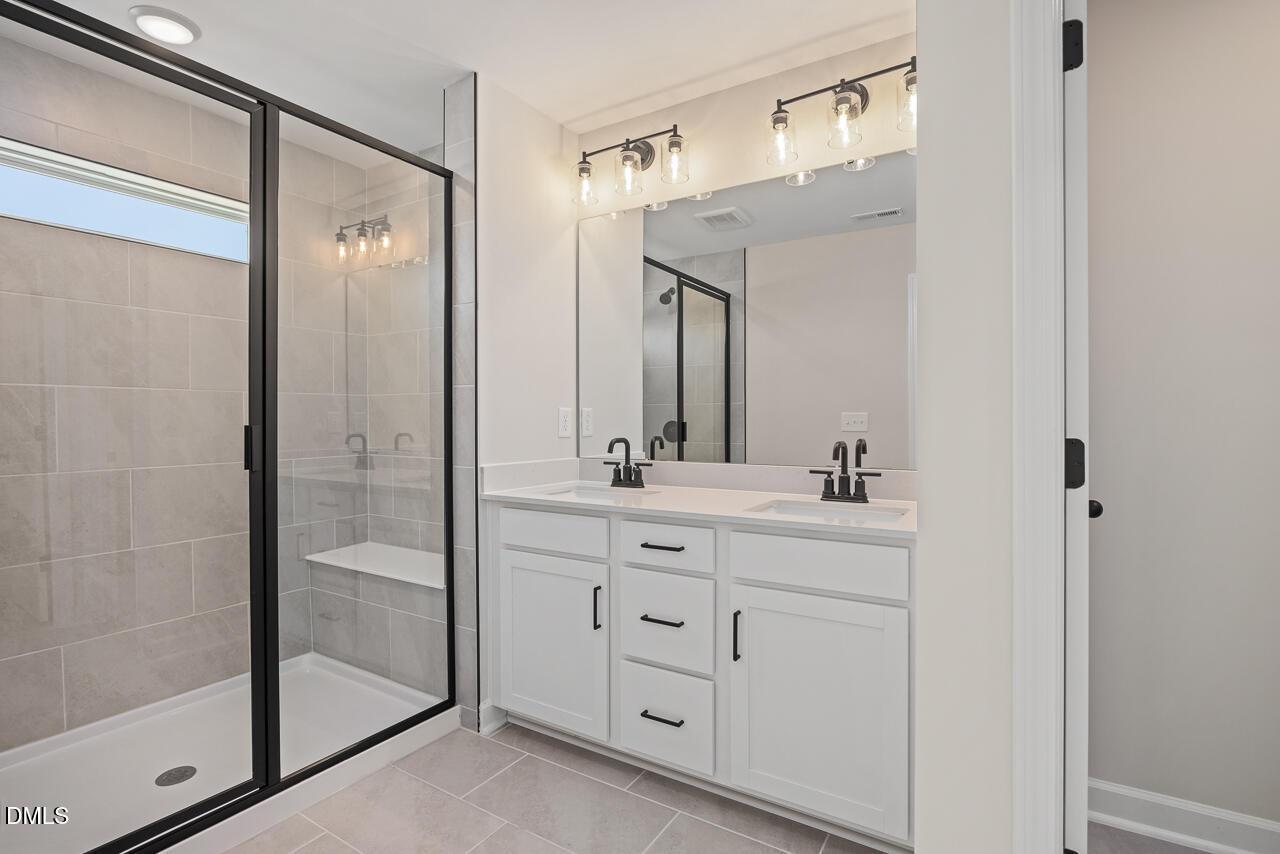 Modern bathroom with double vanity, white cabinets, and walk-in shower in The Mitchell floor plan at Camden Park, Knightdale.