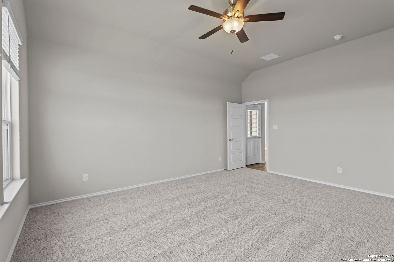 Spacious empty bedroom with gray walls, ceiling fan, large windows, and beige carpet in Davidson Homes The Collin B, Seguin, Texas
