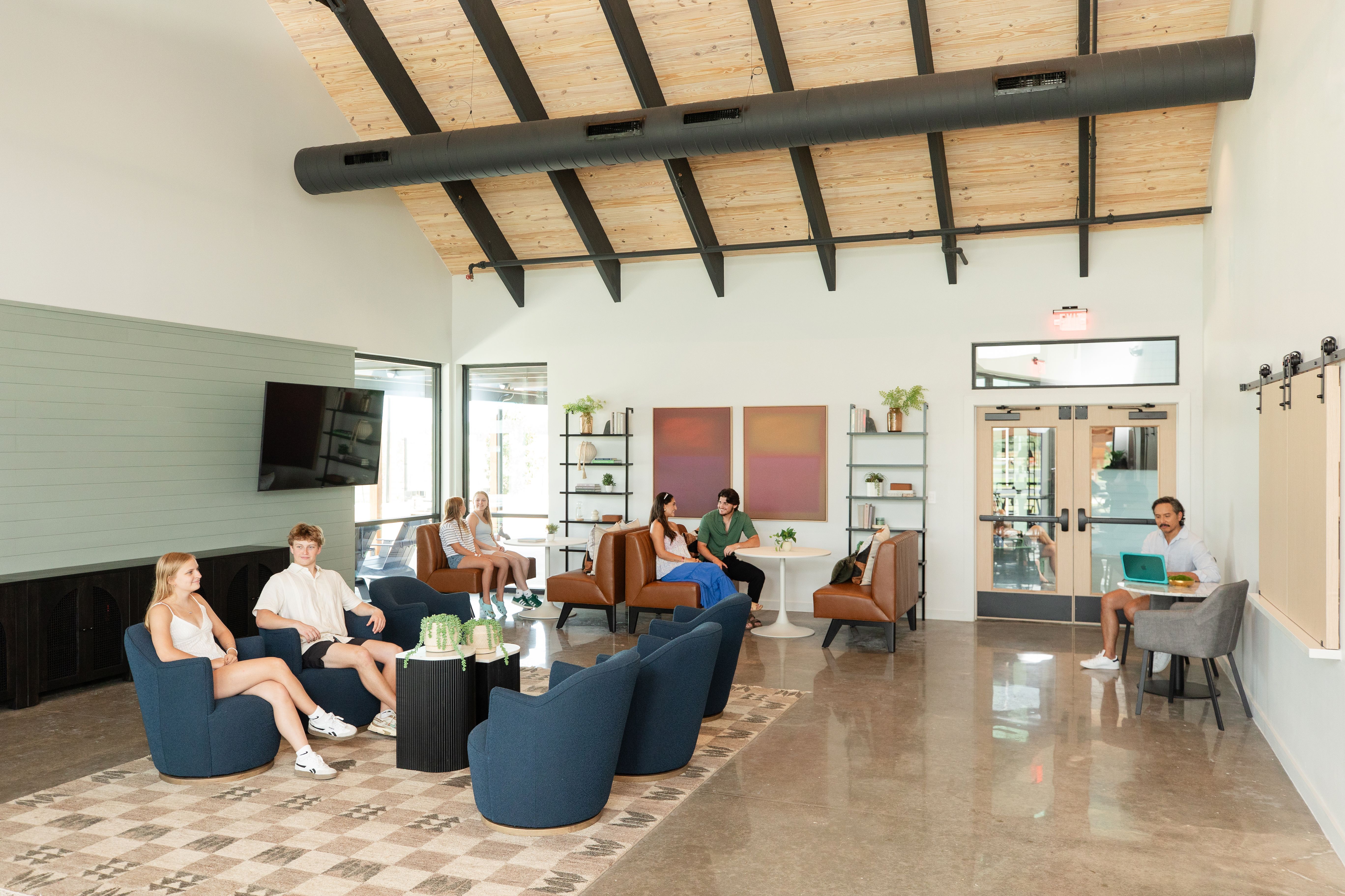 Spacious lounge at Emberly in Beasley Texas with wooden beamed ceiling, blue armchairs, residents chatting, and modern decor