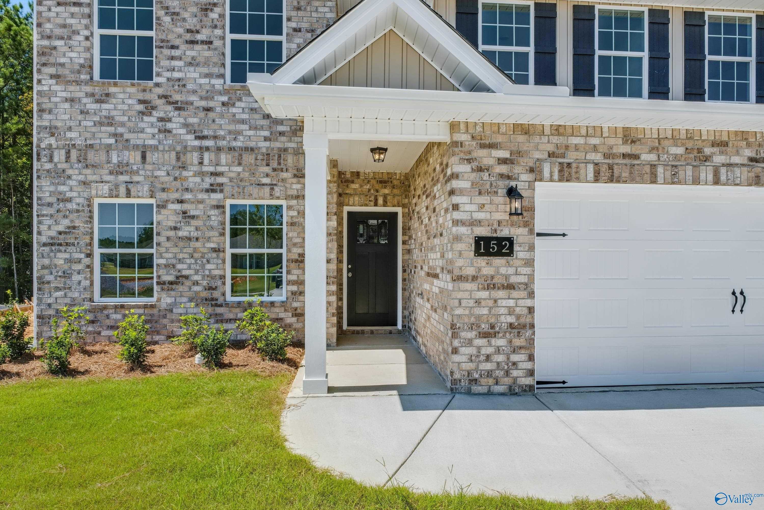 Two-story brick facade of Shelby A home with covered porch, black door #152, 2-car garage, and landscaped yard in The Highlands, Arab, Alabama