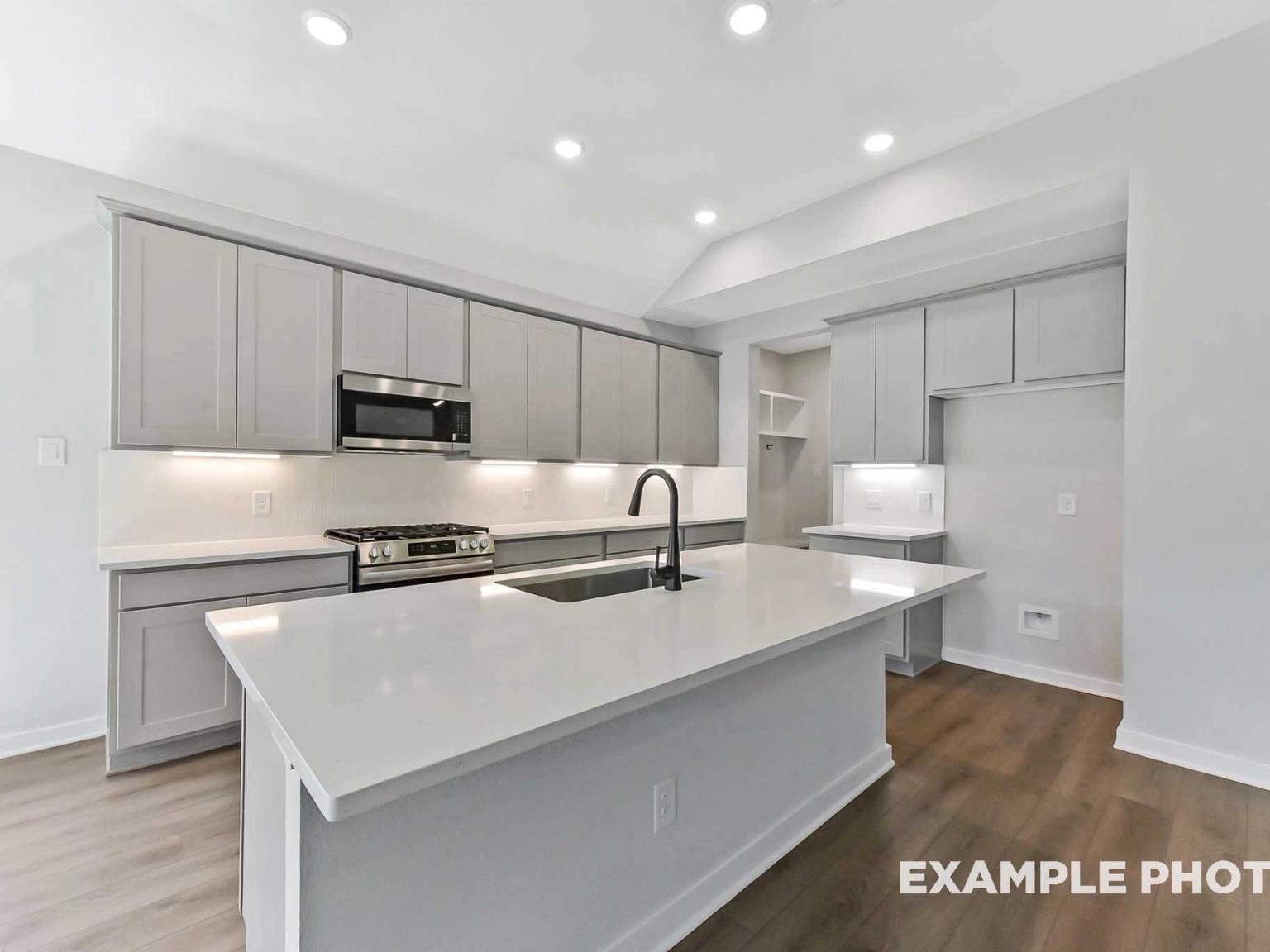 Modern kitchen with quartz island, grey cabinets, and stainless appliances in The Sequoia C plan, Sundance Cove, Crosby, TX.
