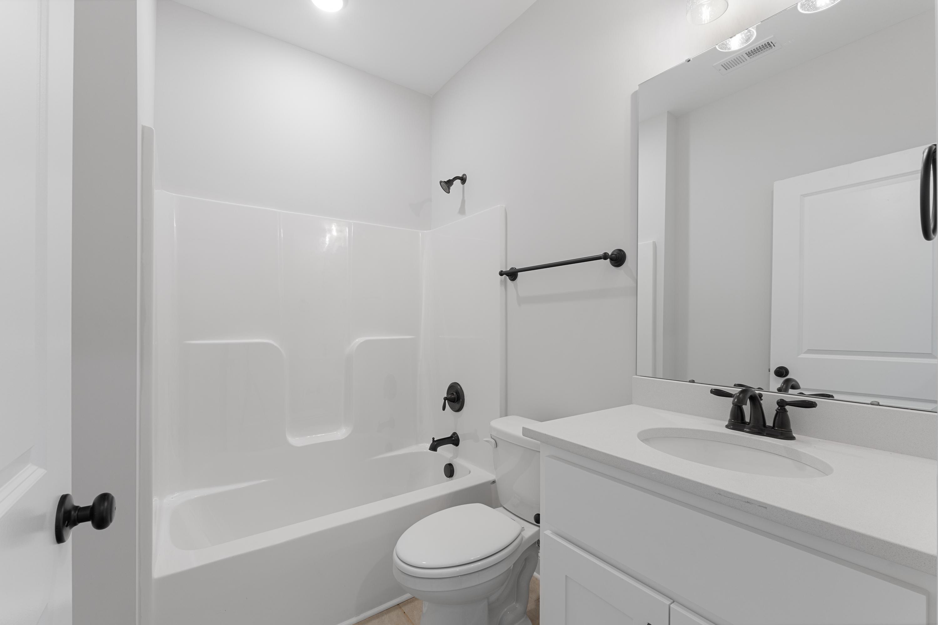 Spacious white bathroom in The Copeland with tub-shower combo, modern vanity sink, toilet, and black fixtures by Davidson Homes