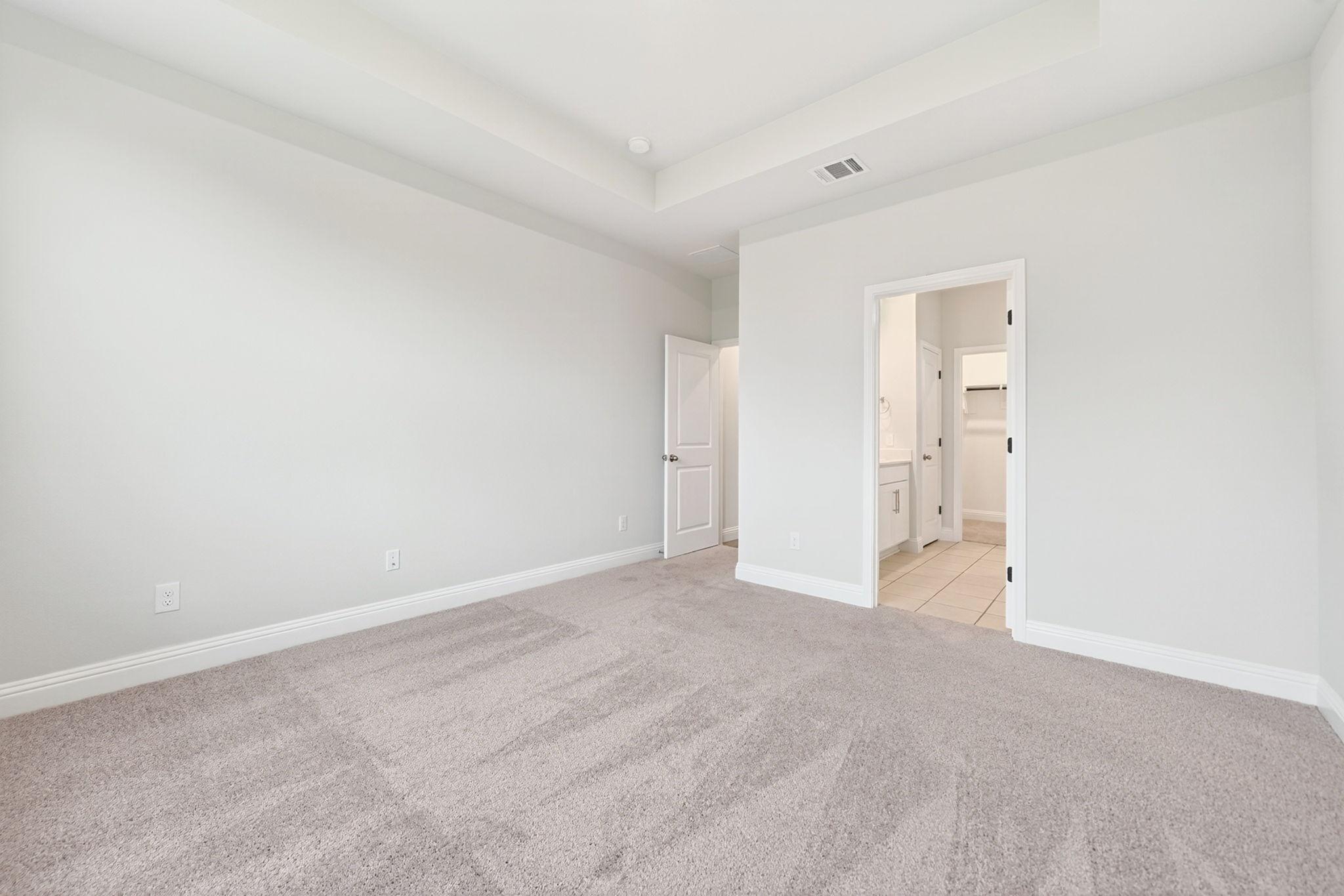 Spacious master suite on the main floor of The Redbud, featuring tray ceilings, neutral carpet, and an en-suite bathroom.