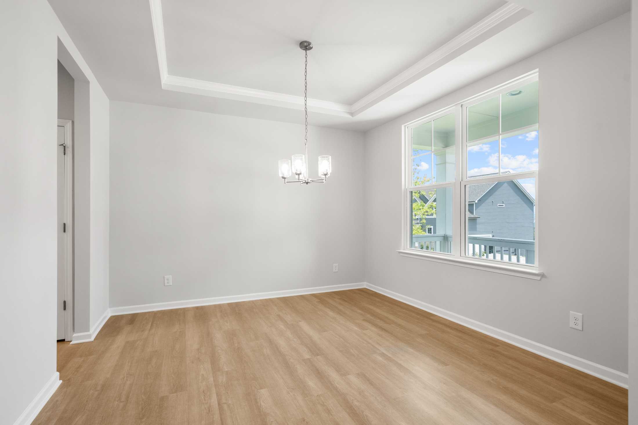 Spacious dining room in The Ash B at Wehunt Meadows with tray ceiling, chandelier, large windows, and hardwood floors in Hoschton GA
