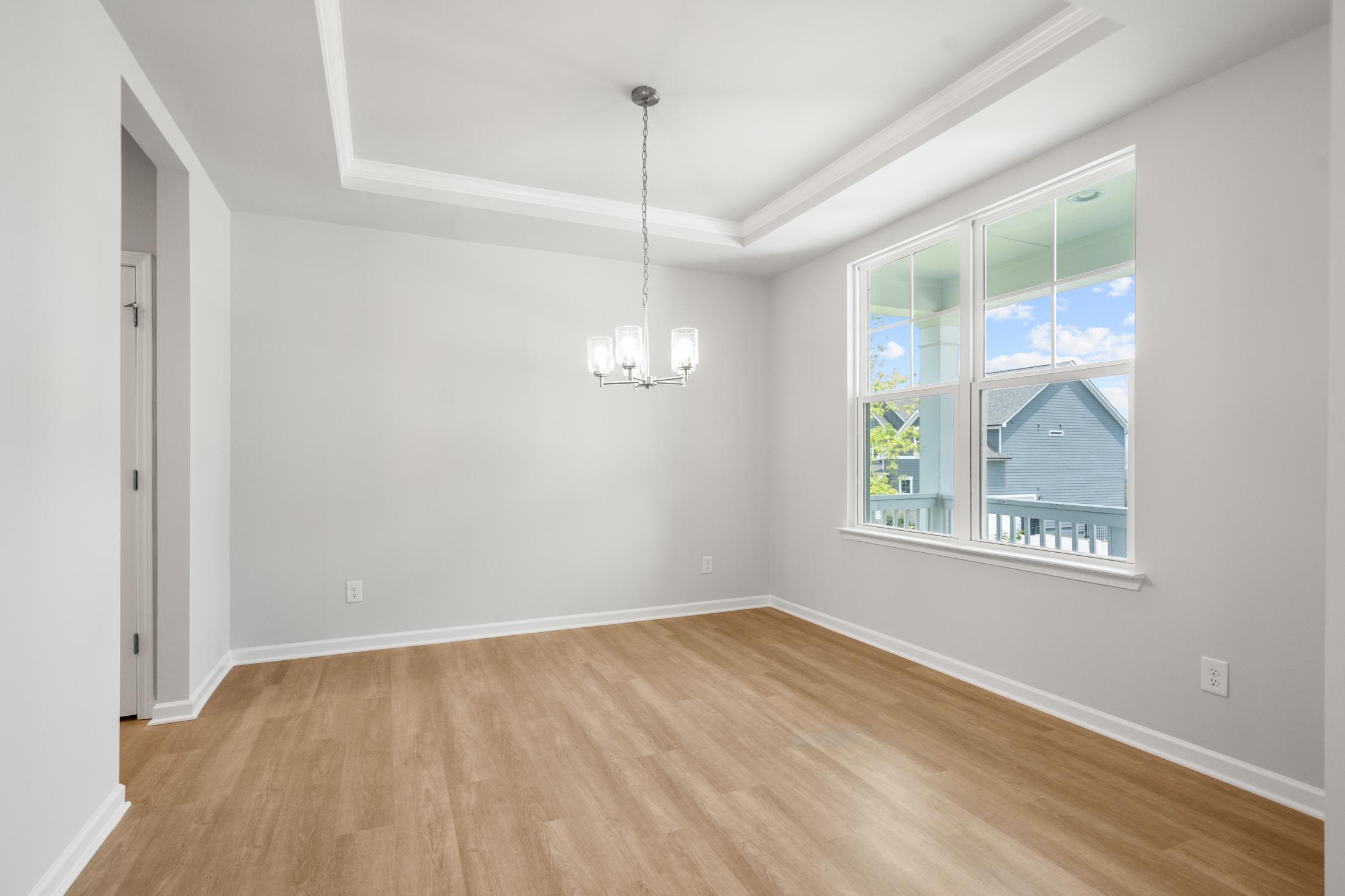 Spacious dining room in The Ash B at Wehunt Meadows with tray ceiling, chandelier, large windows, and hardwood floors in Hoschton GA