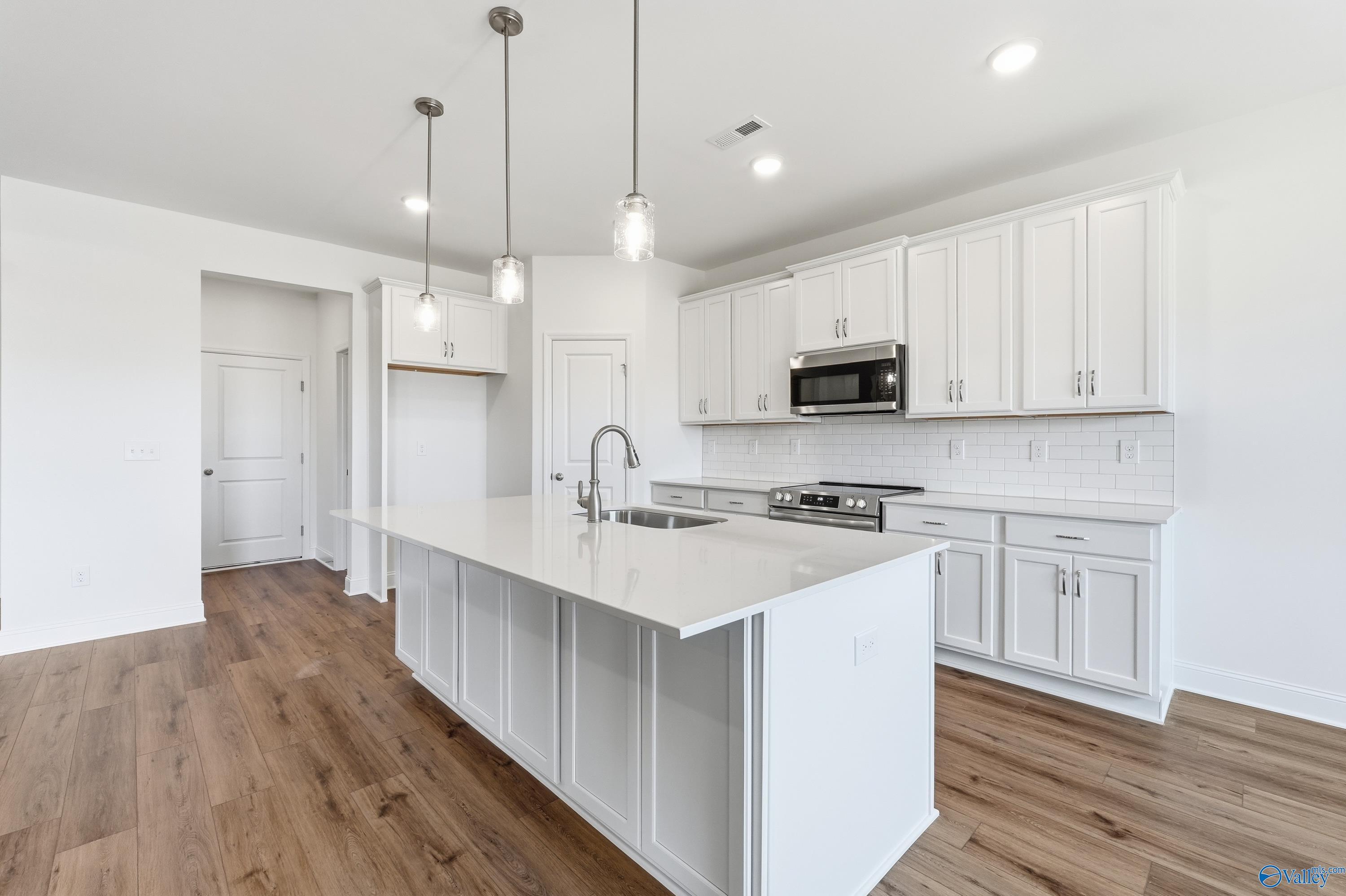 Modern white shaker kitchen with quartz island, stainless appliances, pendant lights in Davidson Homes Montgomery C, Harvest AL