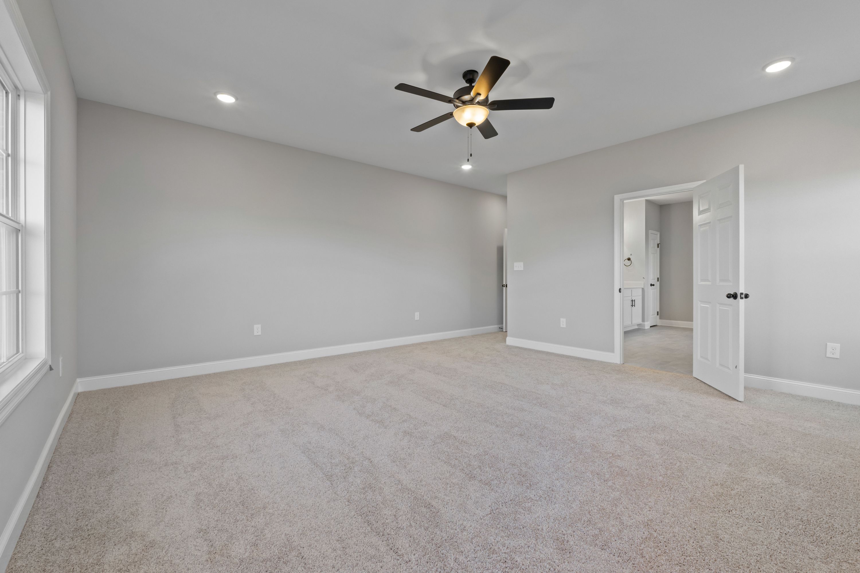 Spacious master bedroom in The Valencia with gray walls, beige carpet, ceiling fan, and ensuite bath door