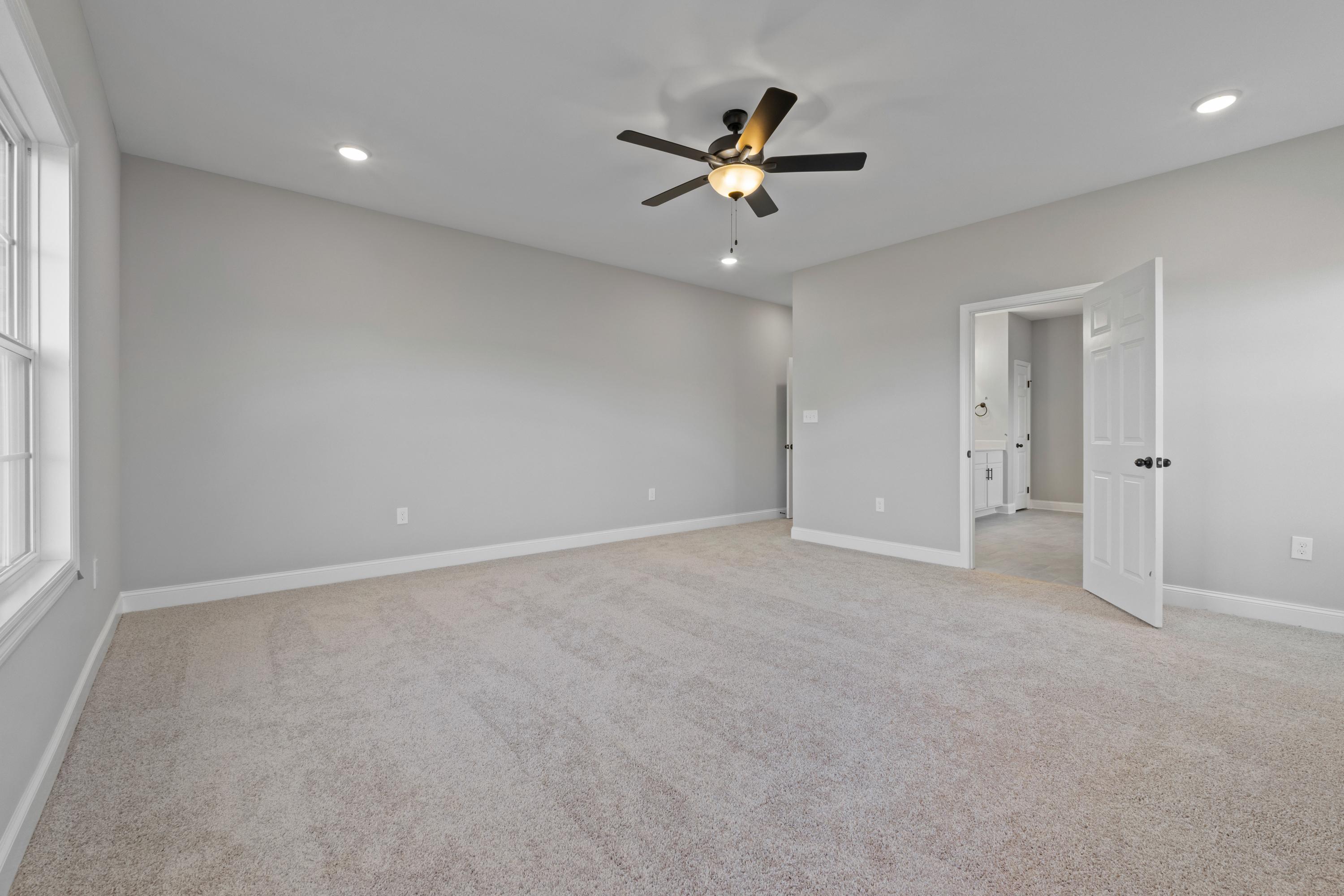 Spacious master bedroom in The Valencia with gray walls, beige carpet, ceiling fan, and ensuite bath door