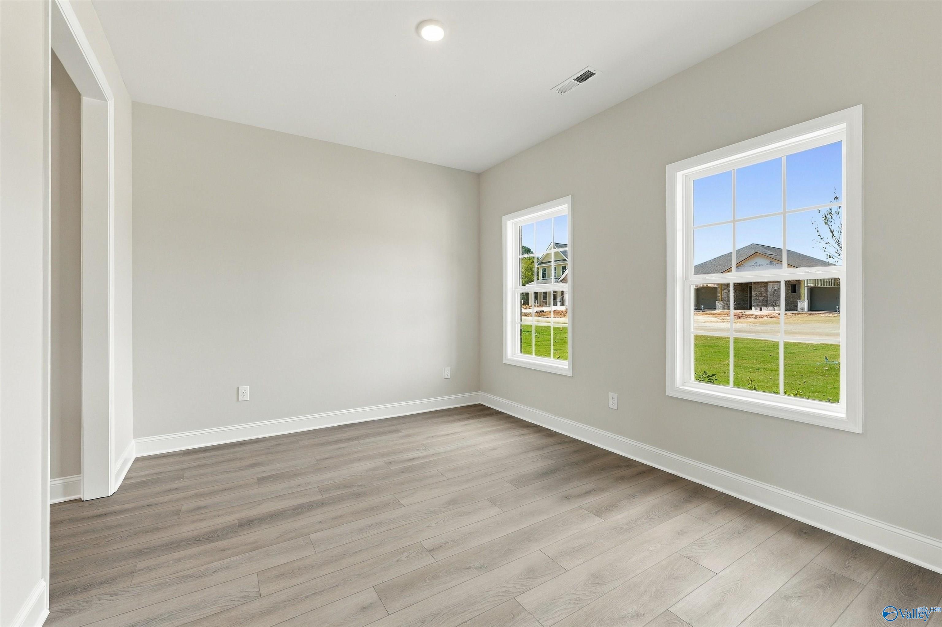 Bright empty bedroom with luxury vinyl plank flooring and large windows in Davidson Homes The Shelby A, The Meadows, Athens, Alabama