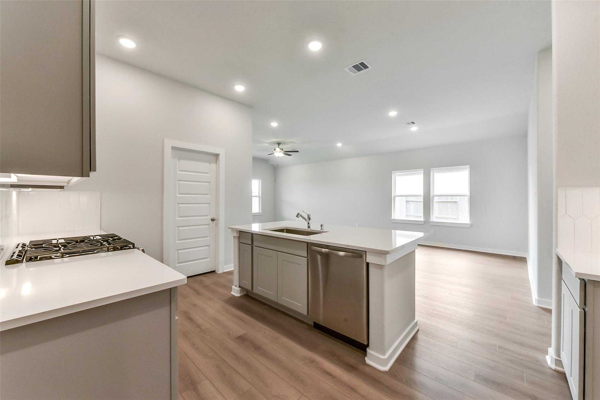 Modern open-concept kitchen with white quartz island, stainless dishwasher, gas cooktop in Davidson Homes The Laguna C, Rosharon, Texas