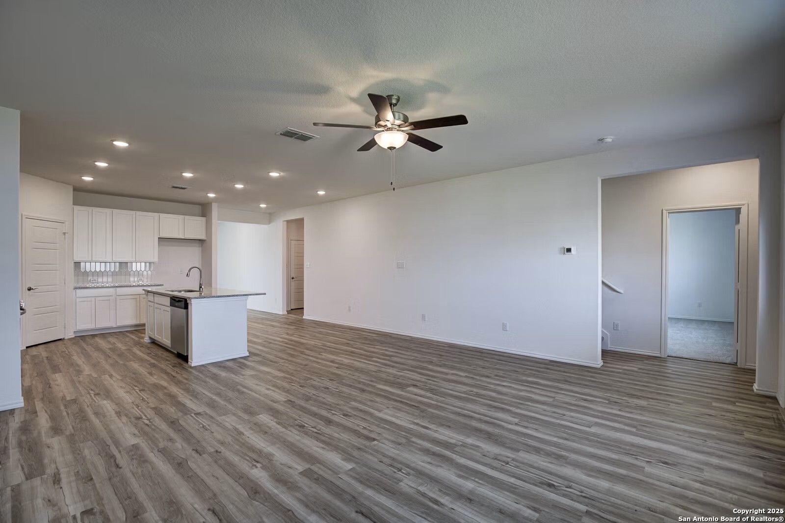 Open-concept kitchen-living area with white cabinets, stainless appliances, large island, and luxury vinyl plank flooring in Davidson Homes The Douglas B, Seguin, Texas
