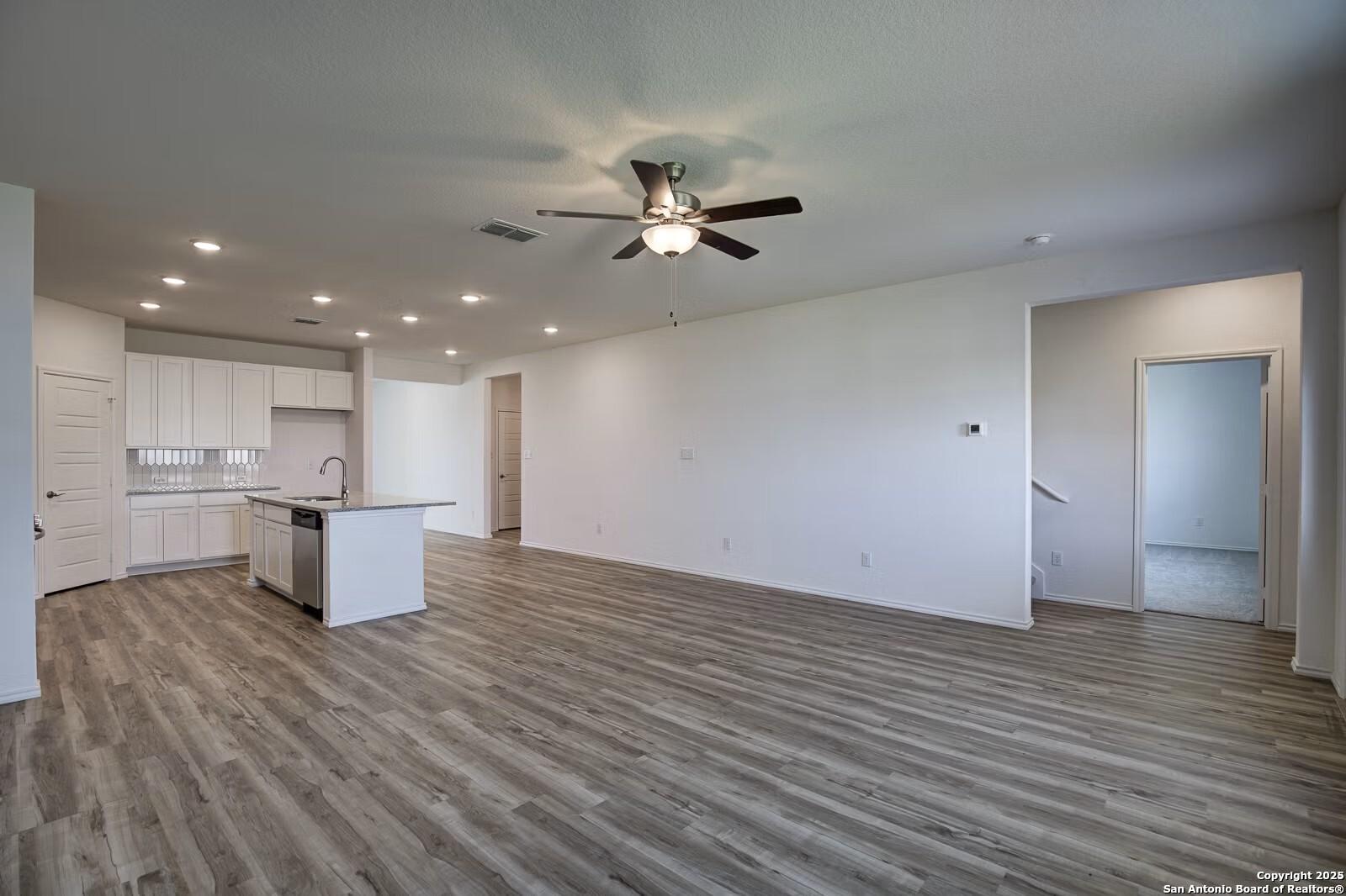 Open-concept kitchen-living area with white cabinets, stainless appliances, large island, and luxury vinyl plank flooring in Davidson Homes The Douglas B, Seguin, Texas