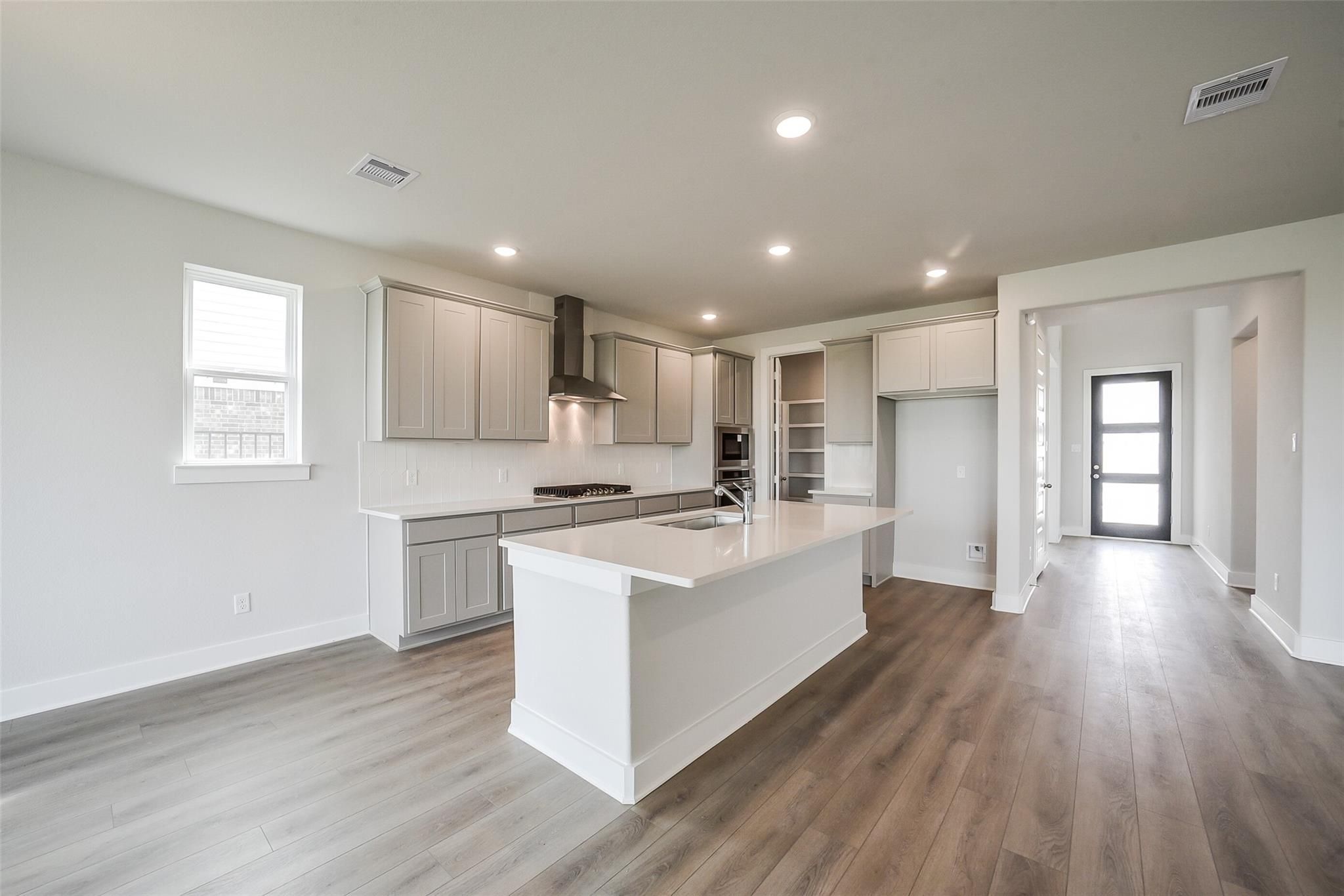 Modern open-concept kitchen with white shaker cabinets, large island, stainless range hood in Davidson Homes The Philip B, Rosharon, Texas