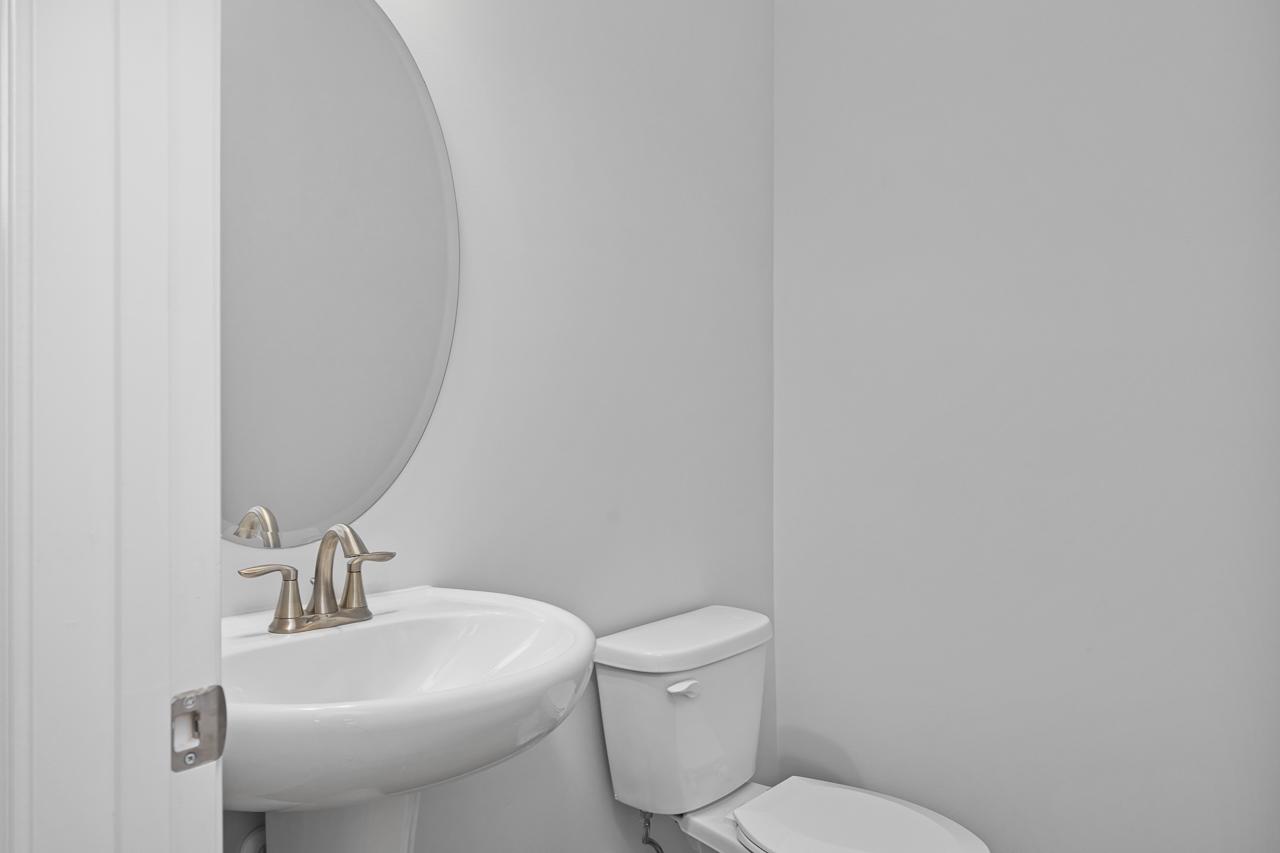 Modern powder room in The Durham C showcasing white pedestal sink, round mirror, and toilet
