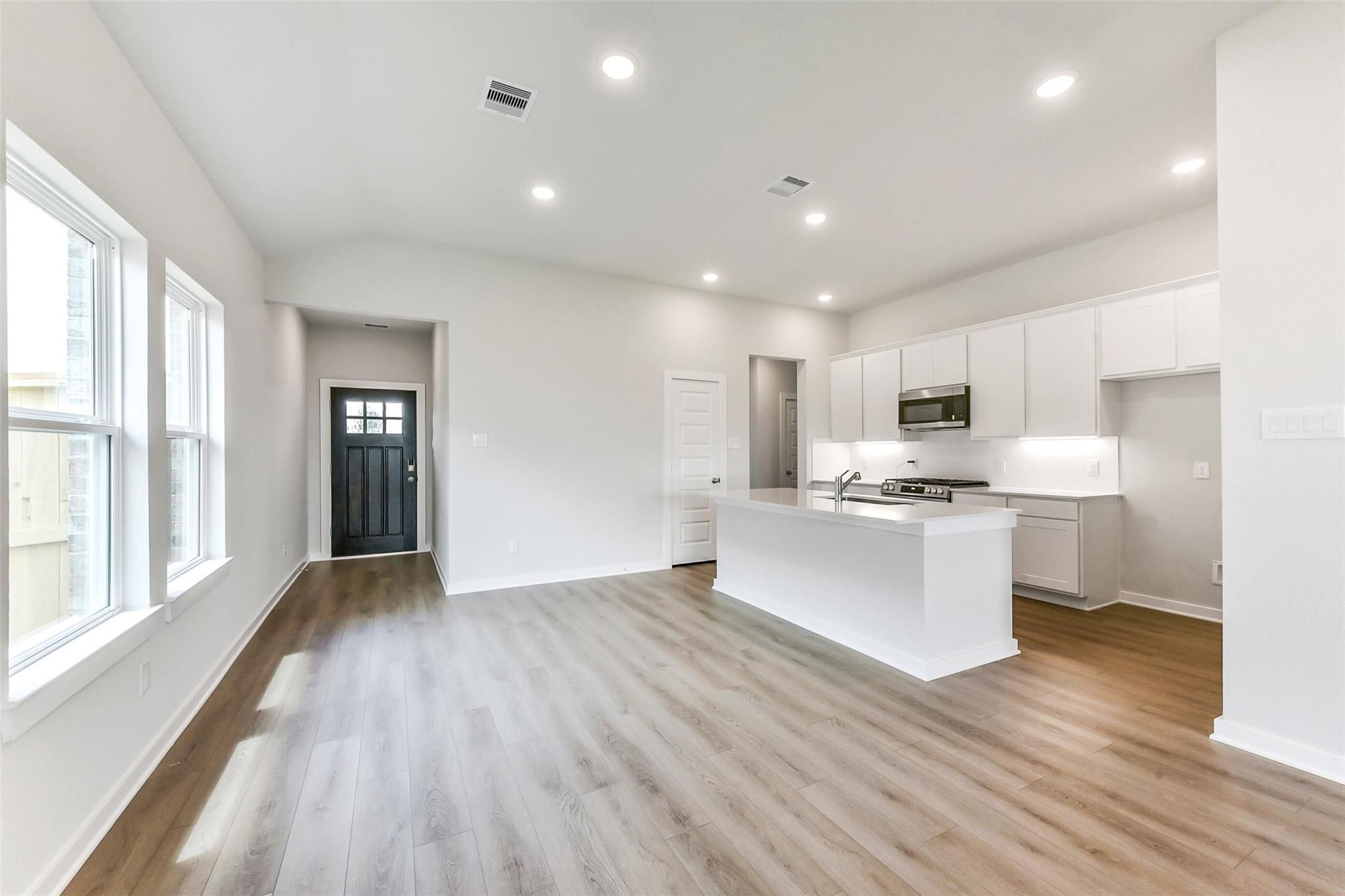 Open-concept kitchen with white cabinets, large island, and light wood floors in Davidson Homes The Costa B, Dayton, Texas