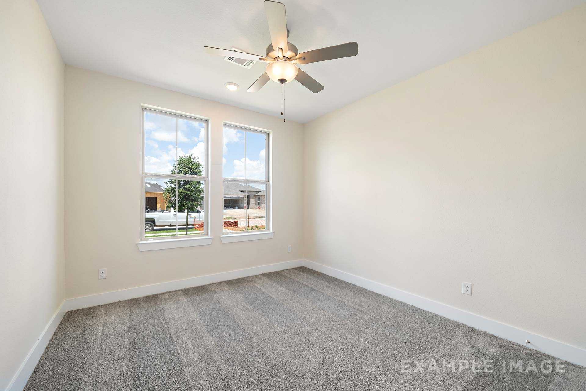 Bright secondary bedroom in The Diana C with large windows overlooking lush yard, ceiling fan, and neutral carpet