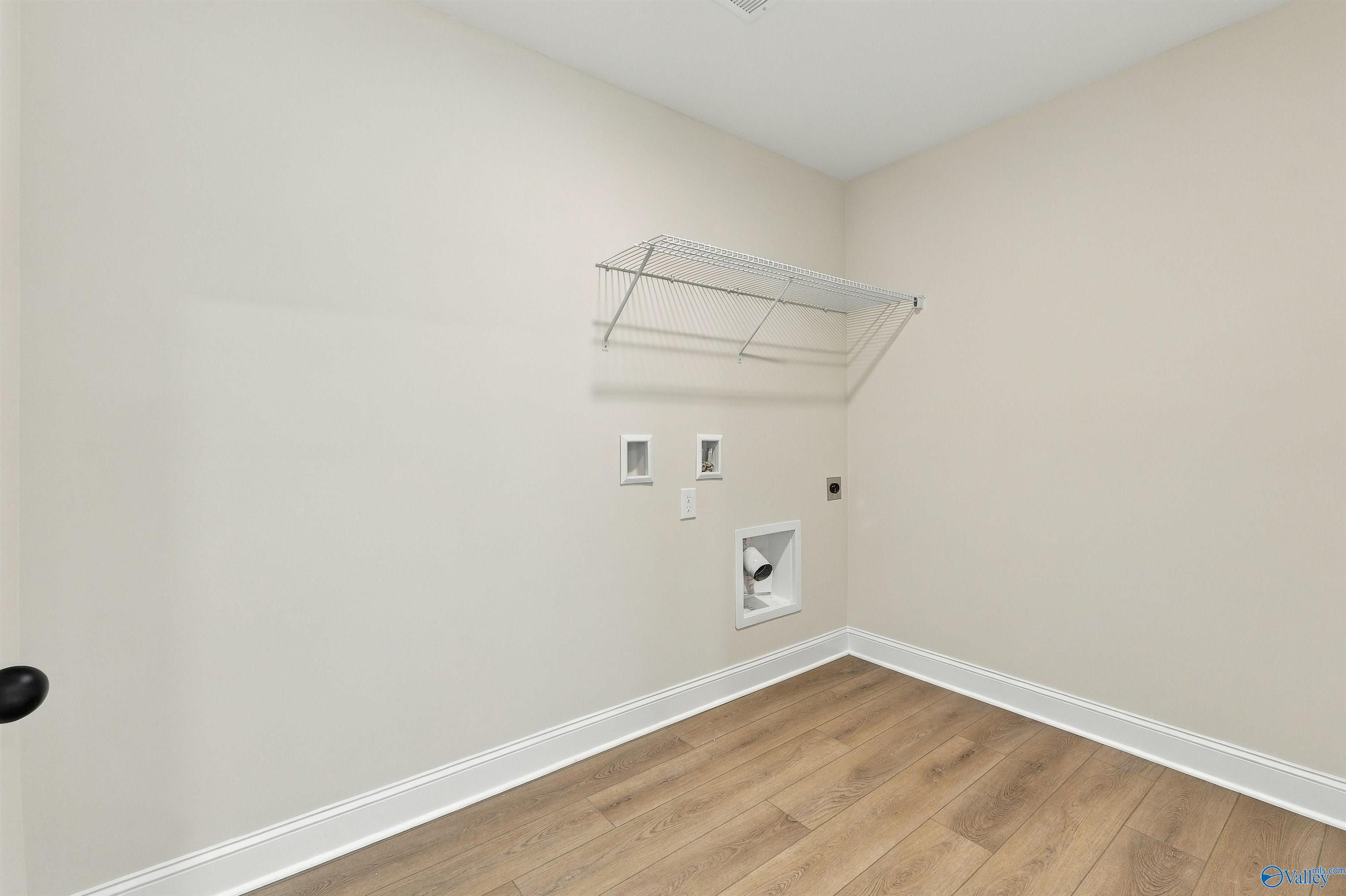 Laundry room with wire shelving, washer hookups, and luxury vinyl plank flooring in Davidson Homes The Shelby A, Athens, Alabama
