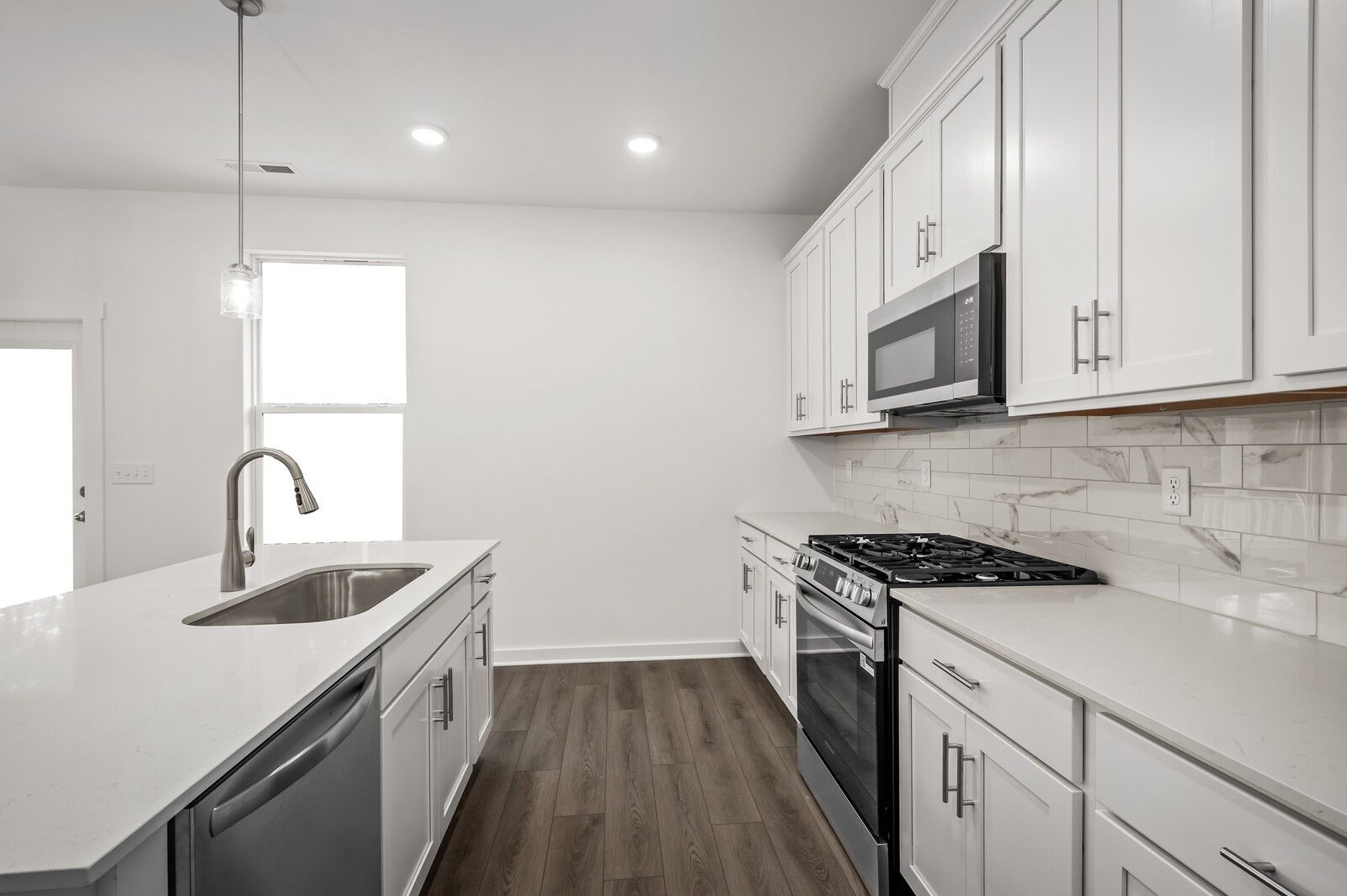 Modern kitchen with white cabinets, quartz countertops, and stainless steel appliances in The Logan C, Calista Farms home.
