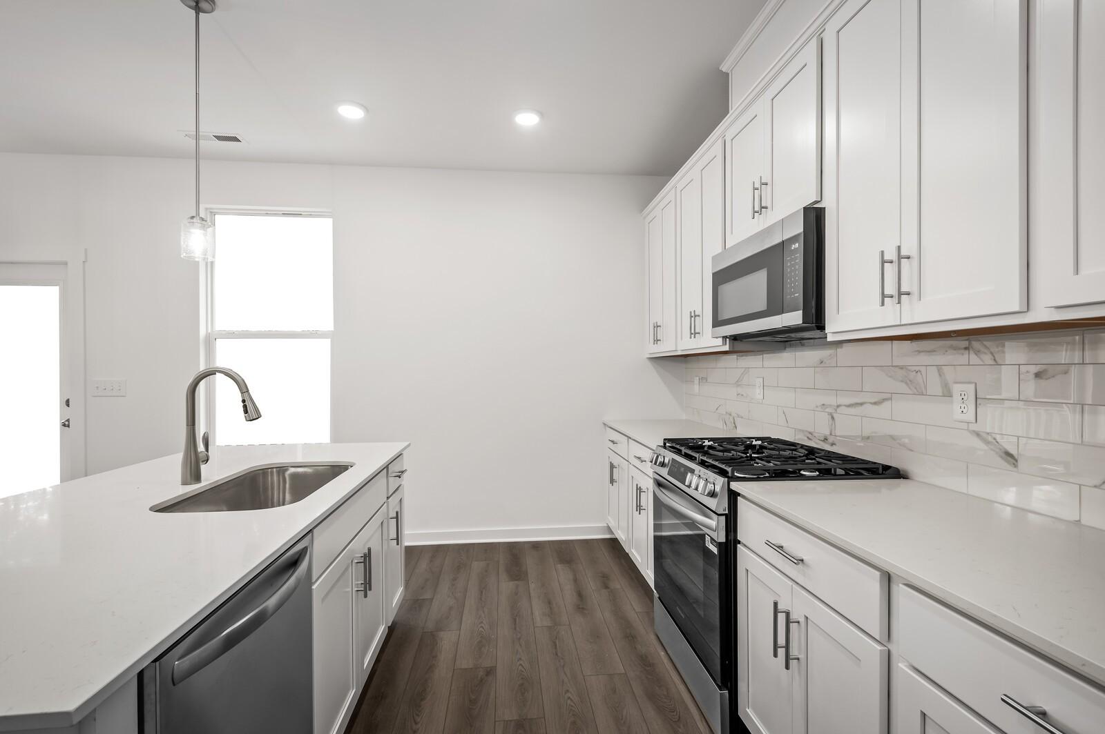 Modern kitchen with white cabinets, quartz countertops, and stainless steel appliances in The Logan C, Calista Farms home.