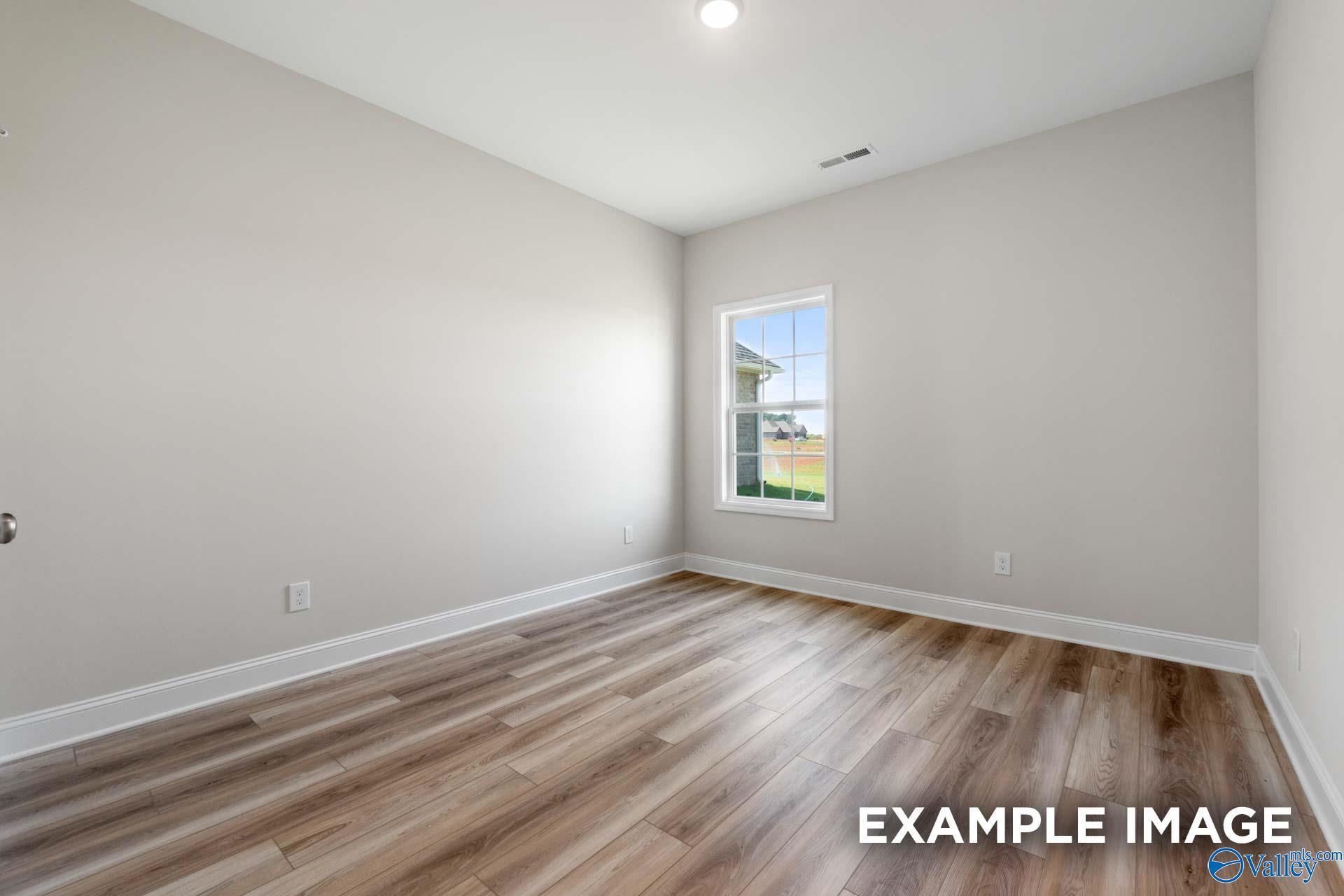 Empty bedroom with light gray walls, large sunny window overlooking lawn, luxury vinyl plank flooring in The Madison A home, Toney, Alabama