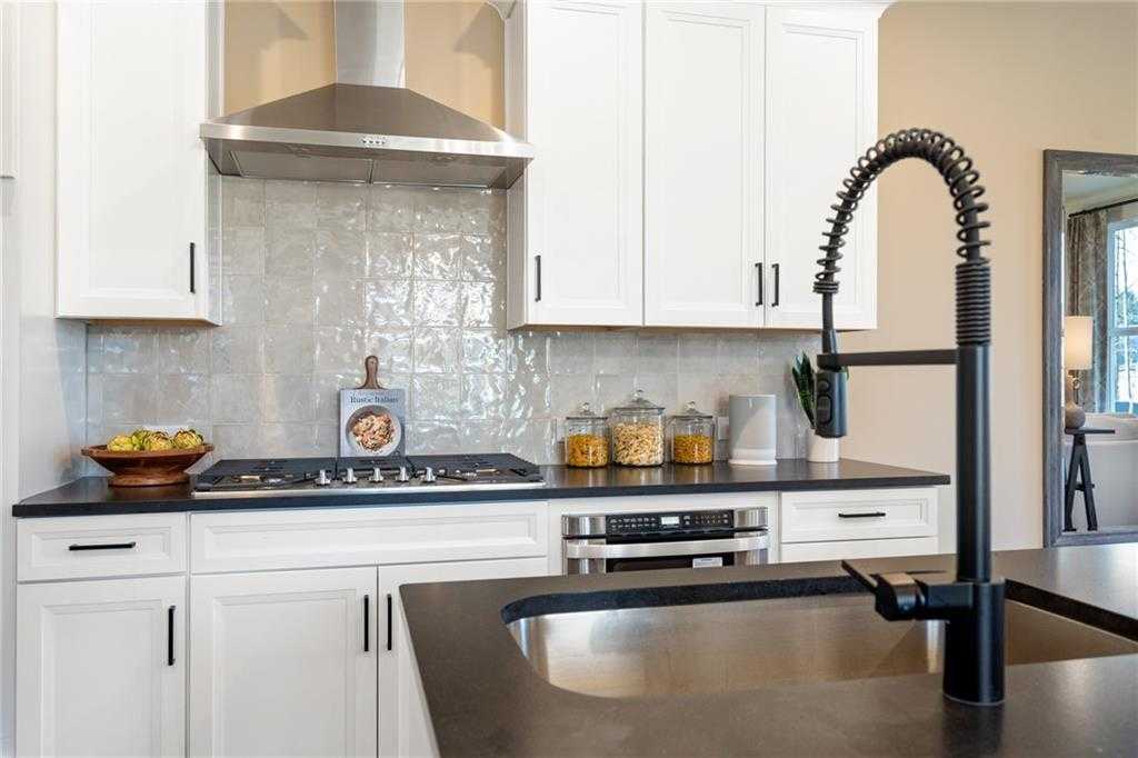 Modern white kitchen with subway tile backsplash, black faucet, stainless range hood in The Marion C by Davidson Homes, Winder, GA