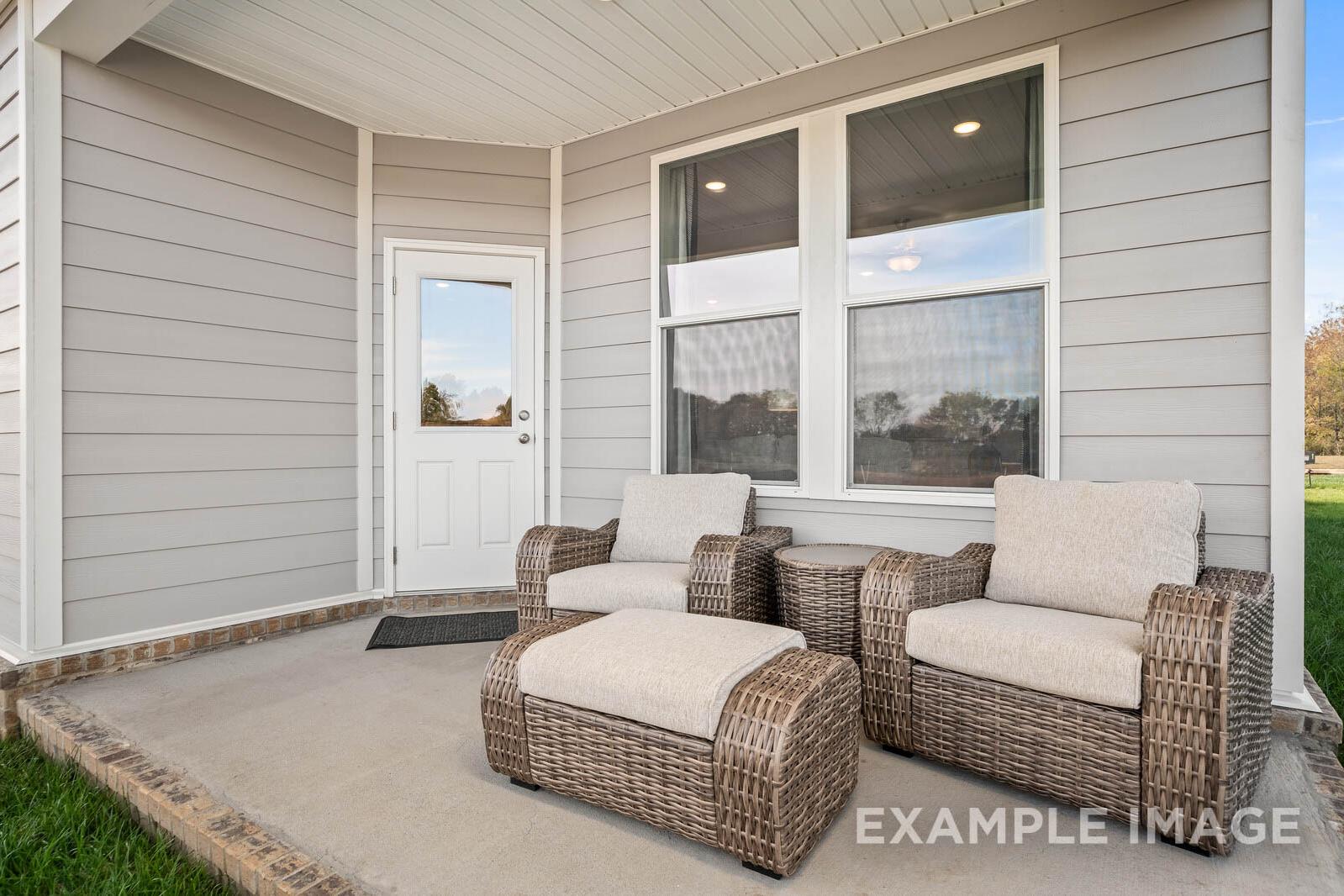 Spacious covered patio of The Franklin B showcasing wicker chairs, ottoman, and large windows in Davidson Homes design