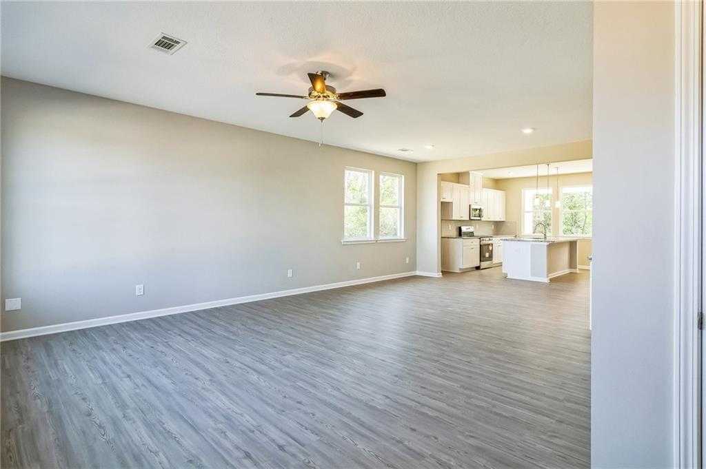 Open-concept living room with ceiling fan, beige walls, and adjacent white kitchen island in The Stella home, Perry, Georgia