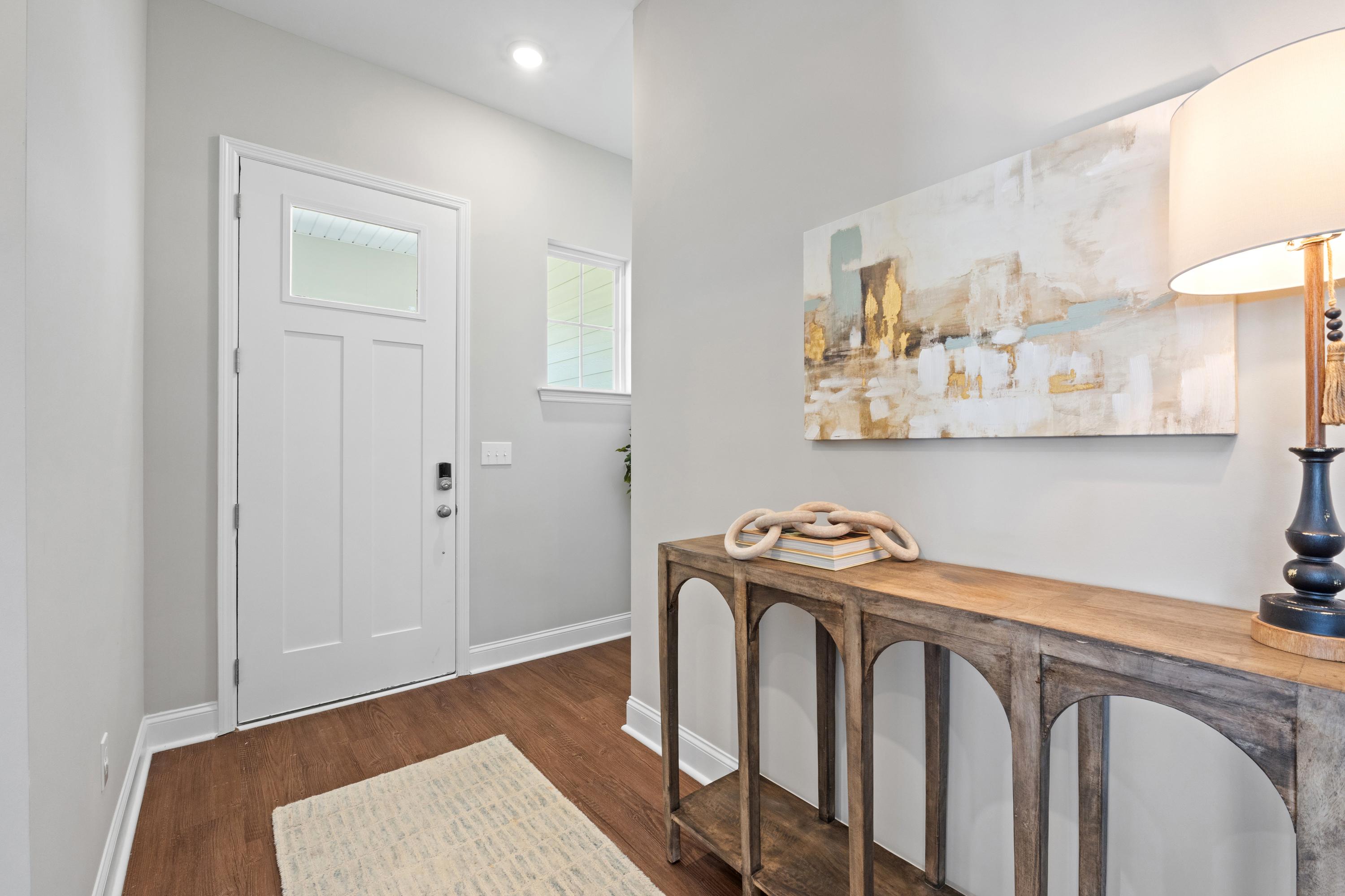 Welcoming entry foyer in The Haven by Evermore Homes featuring white glass-paneled door, abstract wall art, and wooden console with lamp