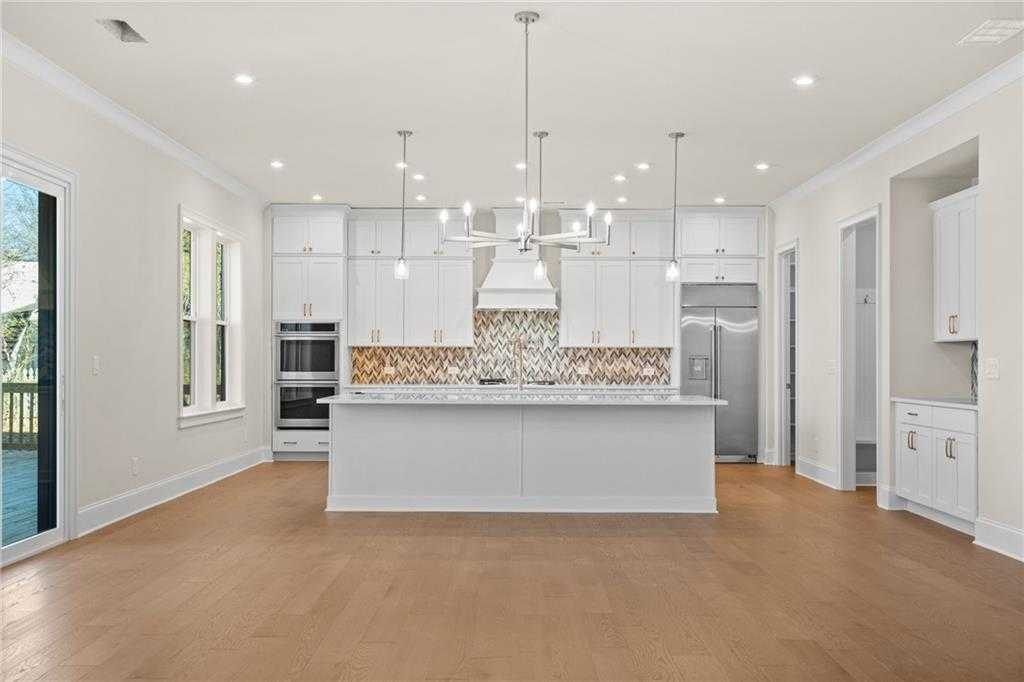 Modern white kitchen with large center island, stainless steel appliances, mosaic backsplash, and pendant lights in Davidson Homes The Arlington A, East Cobb, Georgia