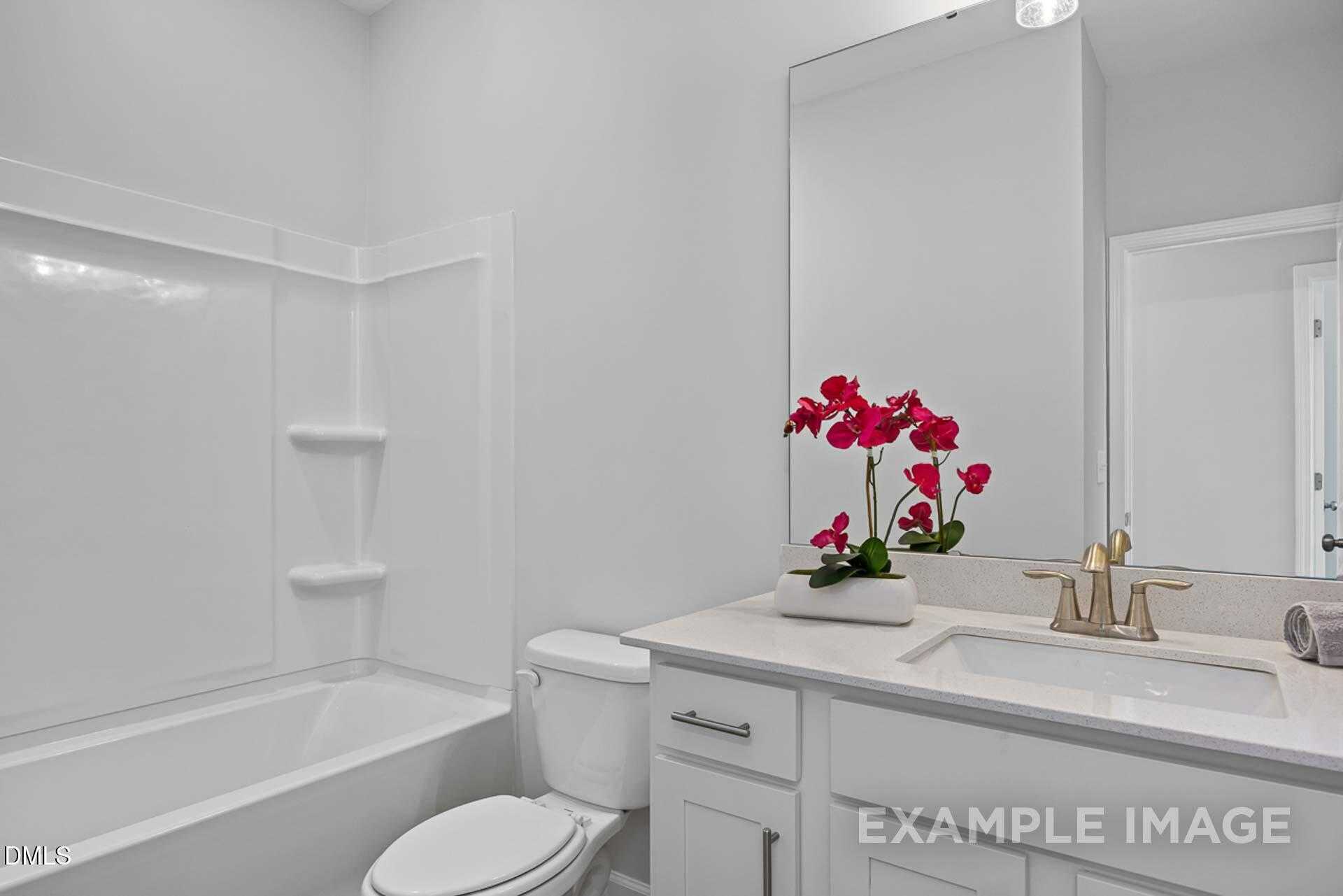 Bright white full bathroom with bathtub, walk-in shower, single vanity sink, and red orchids in Davidson Homes The Carter C, Lillington, NC