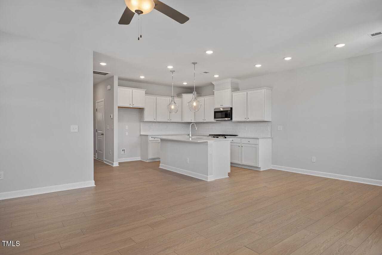 Modern open-concept kitchen with white cabinets, large island sink, pendant lights, and hardwood floors in Davidson Homes The Graham, Fuquay-Varina, NC