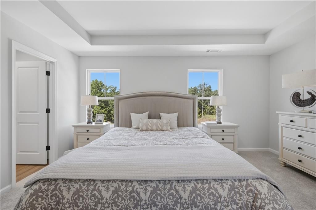 Bright owner's bedroom with tray ceiling, upholstered headboard, and white nightstands in Davidson Homes Hartwell C, Canton GA