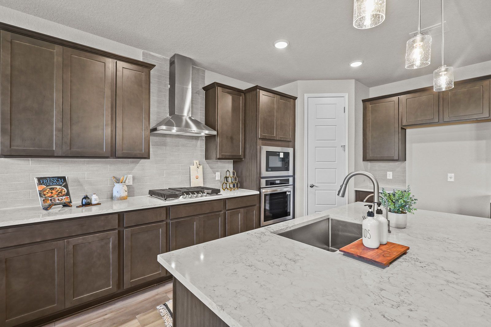 Modern kitchen in The Jennings G featuring dark wood cabinets, quartz countertops, a large island, and stainless appliances.