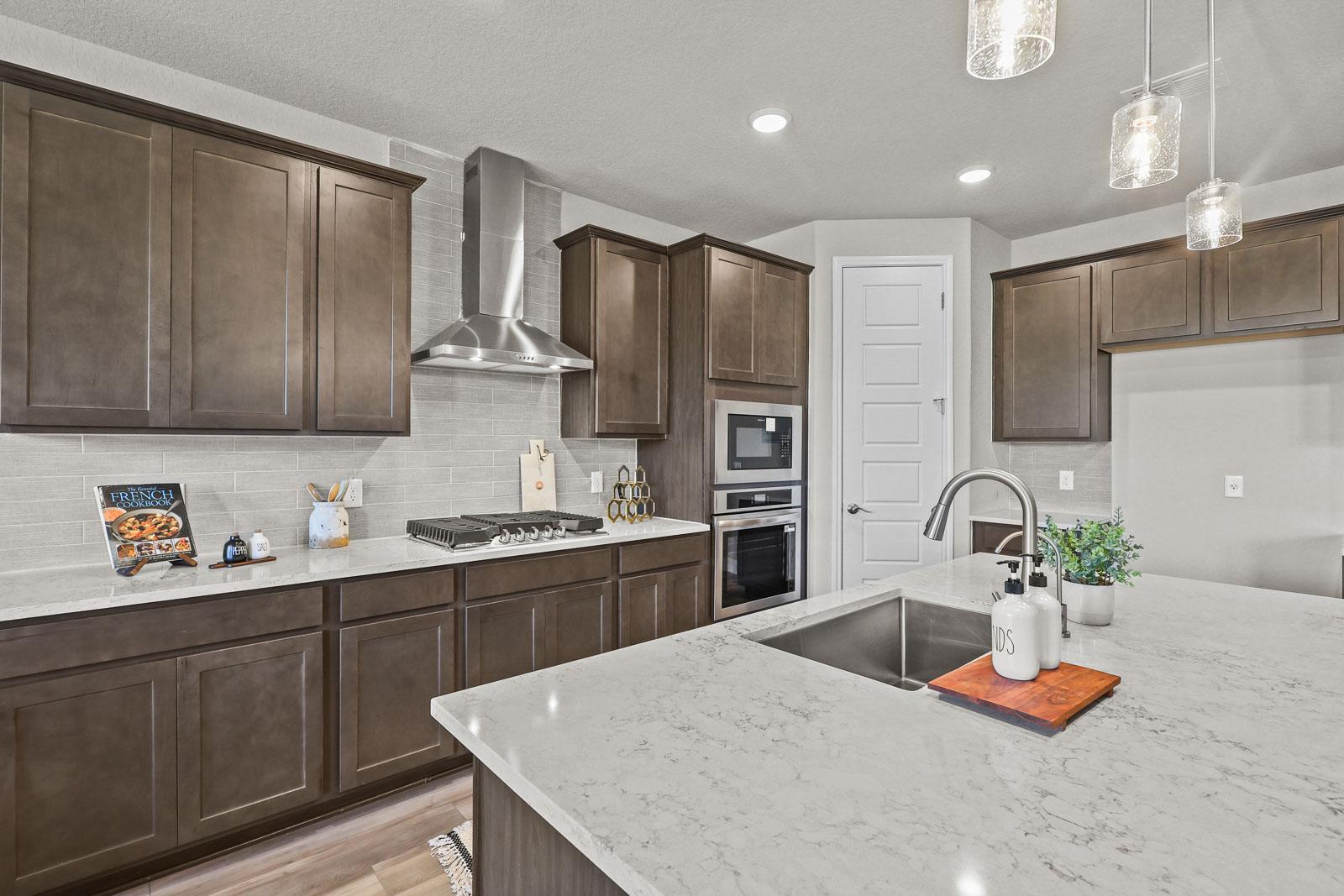 Modern kitchen in The Jennings G featuring dark wood cabinets, quartz countertops, a large island, and stainless appliances.