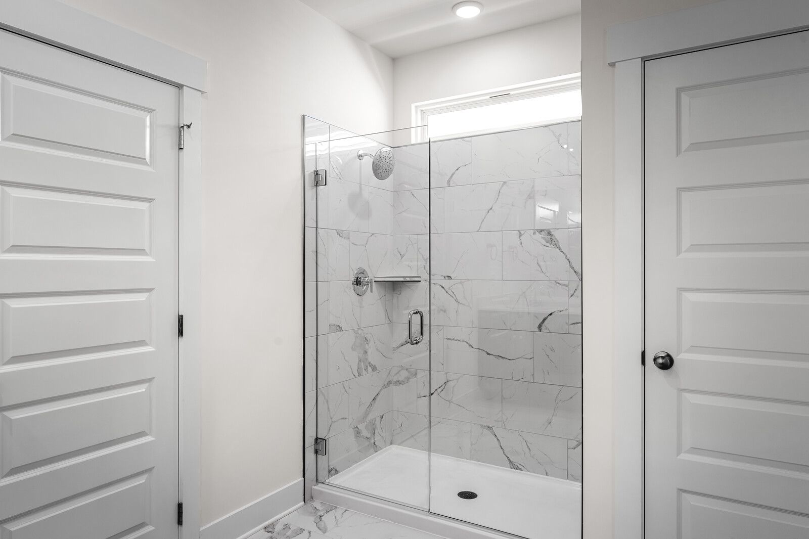 Modern master bathroom shower in The Cottonwood featuring marble-look tile, glass door, and premium fixtures.