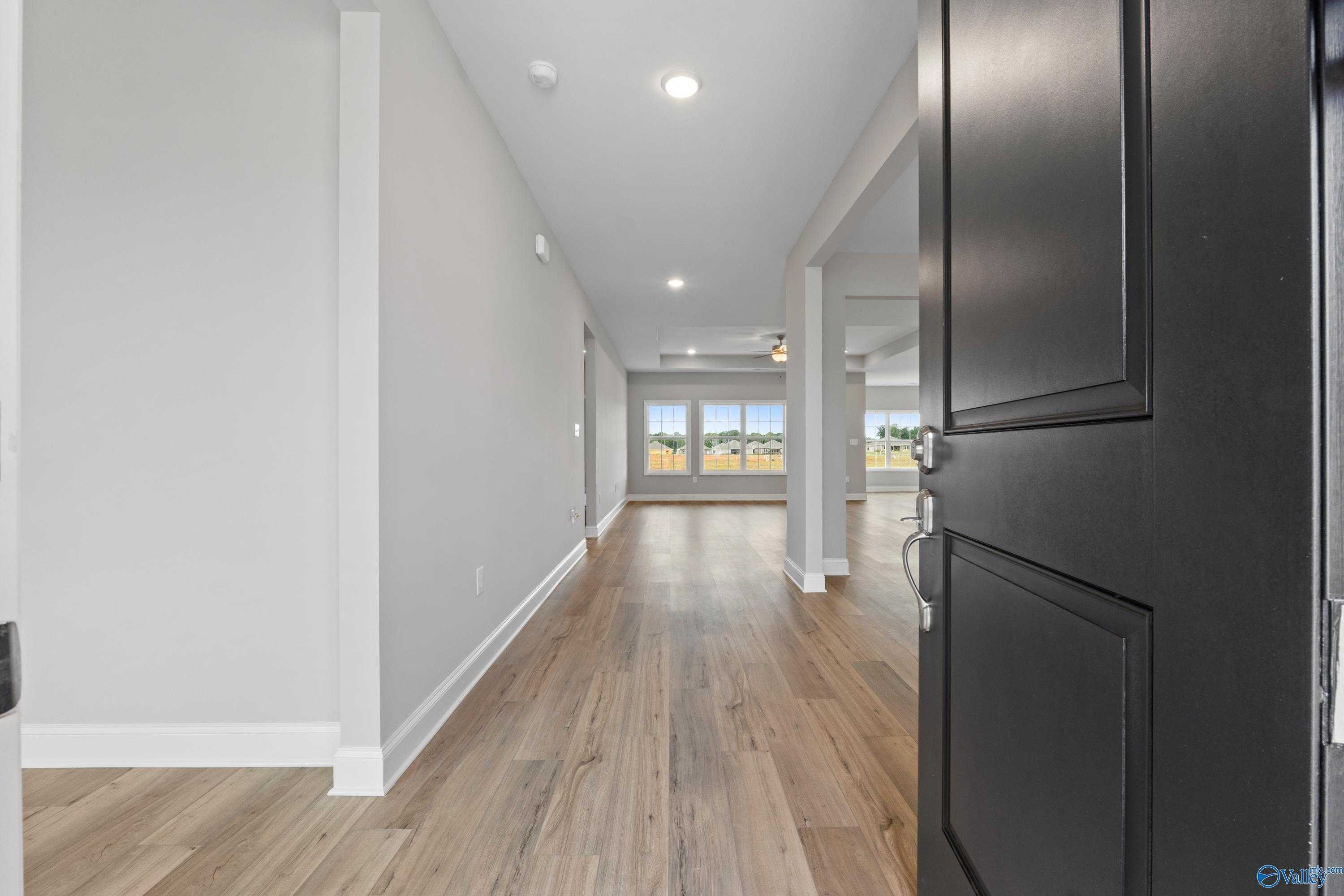 Wide hallway with light hardwood floors, white walls, and open black door to sunlit windows in Davidson Homes The Finleigh, Meridianville, Alabama