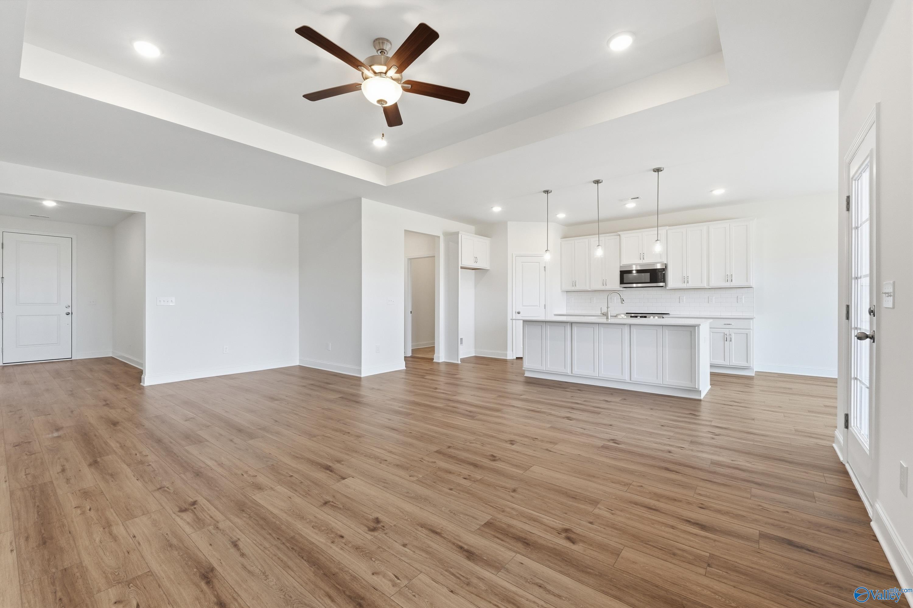 Open-concept kitchen and living area with hardwood floors, white island cabinets, pendant lights, and ceiling fan in Davidson Homes Montgomery C, Harvest, AL
