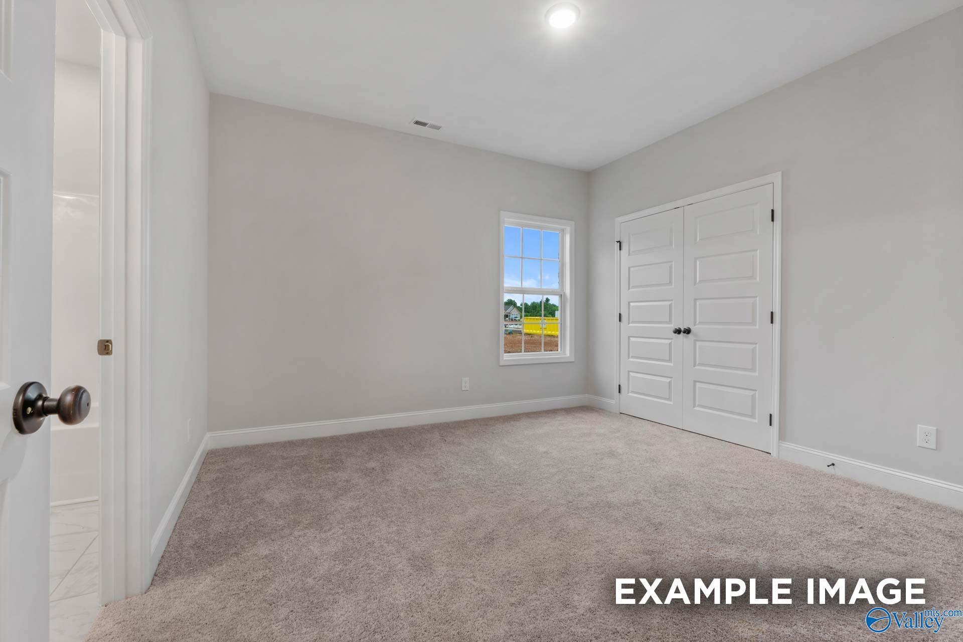 Bright bedroom with gray walls, beige carpet, large window, and double closet doors in Davidson Homes The Finleigh, Meridianville, Alabama