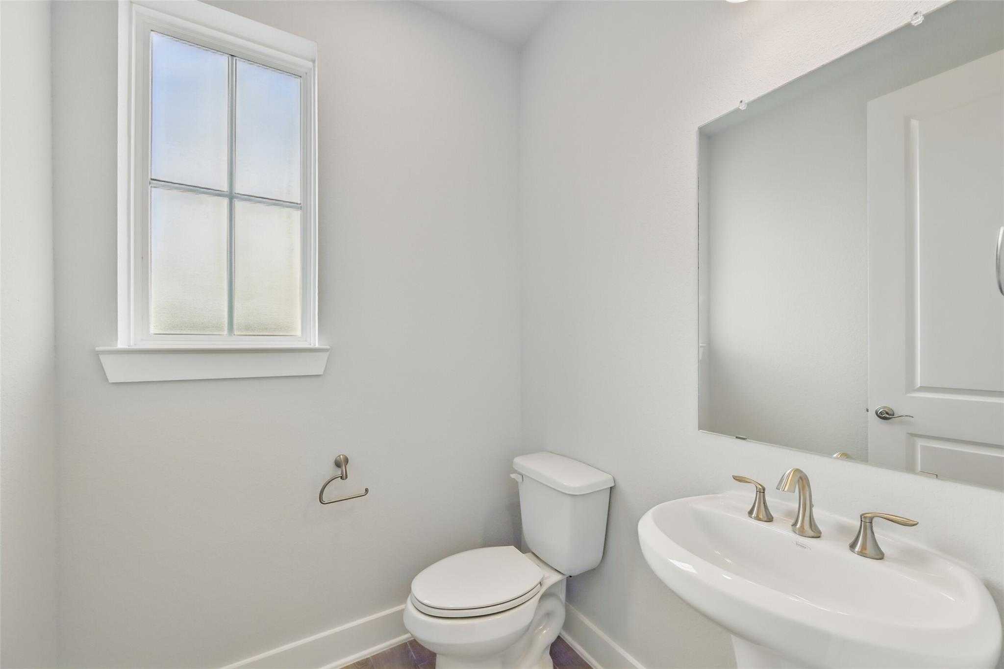 Modern half bathroom with white porcelain sink, toilet, chrome faucet, mirror, and frosted window in Davidson Homes The Philip A, Lago Mar, Texas City