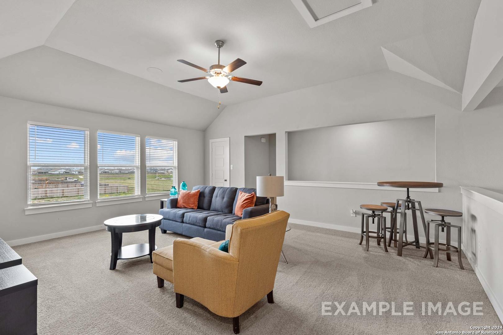 Bright living room with vaulted ceiling, ceiling fan, navy sofa, and large windows overlooking fields in The Collin A home, Seguin, Texas